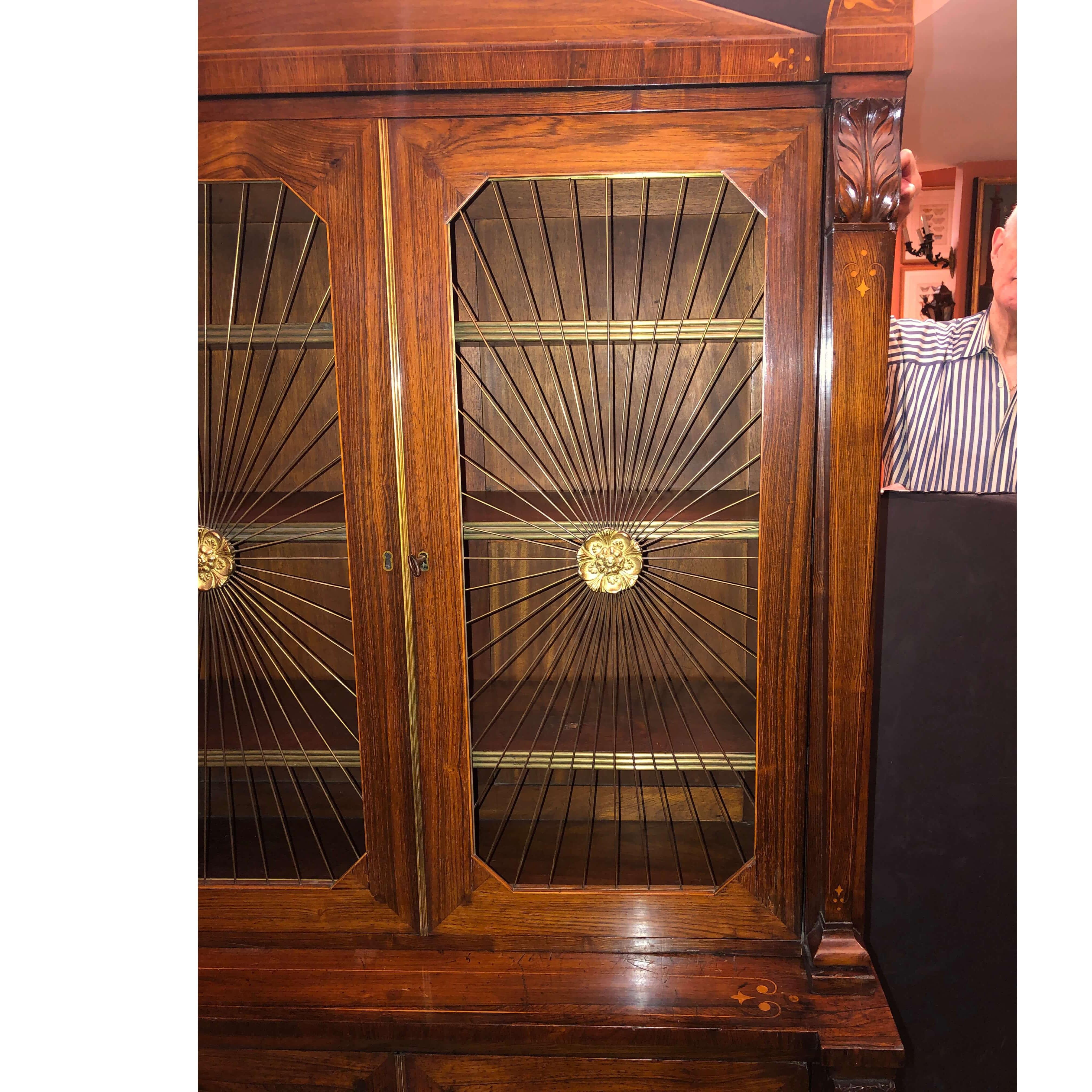 An unusual petite Regency rosewood grill door bookcase in the Neo Egyptian style with pediment top, satinwood line inlay and palmettes with brass trim, brass grills and rondelles. The lower cabinet with paneled closed doors also having satinwood