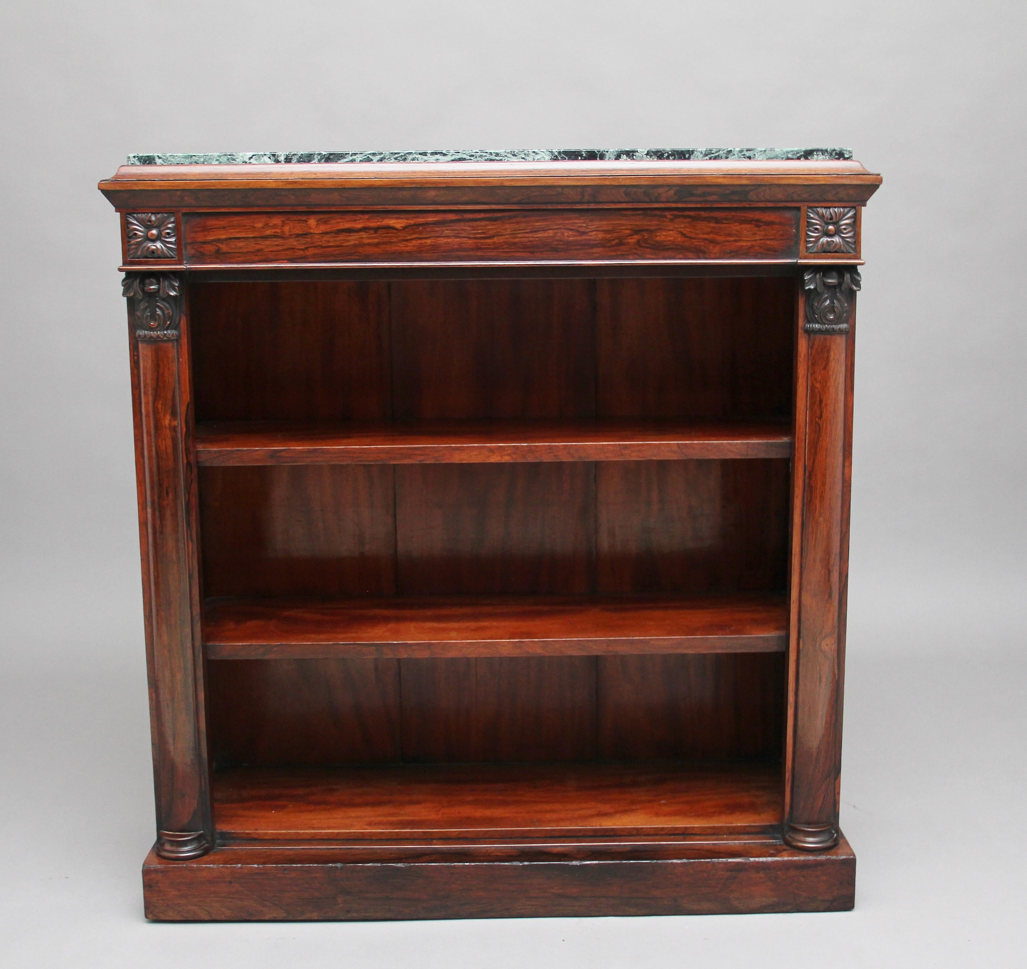 Early 19th century rosewood open bookcase, the top surmounts with a later green veined marble top, having a frieze below with carved decoration either end, the bookcase having two adjustable shelves flanked by carved capital column supports, raised