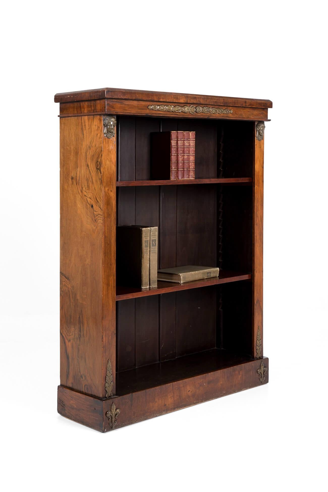 Elegant Regency rosewood open bookcase on a raised plinth base. With decorative ormolu mounts framing the two height-adjustable shelves. Ormolu mounts consisting of a central floral scrolling motif flanked below by two classical maiden figures. The