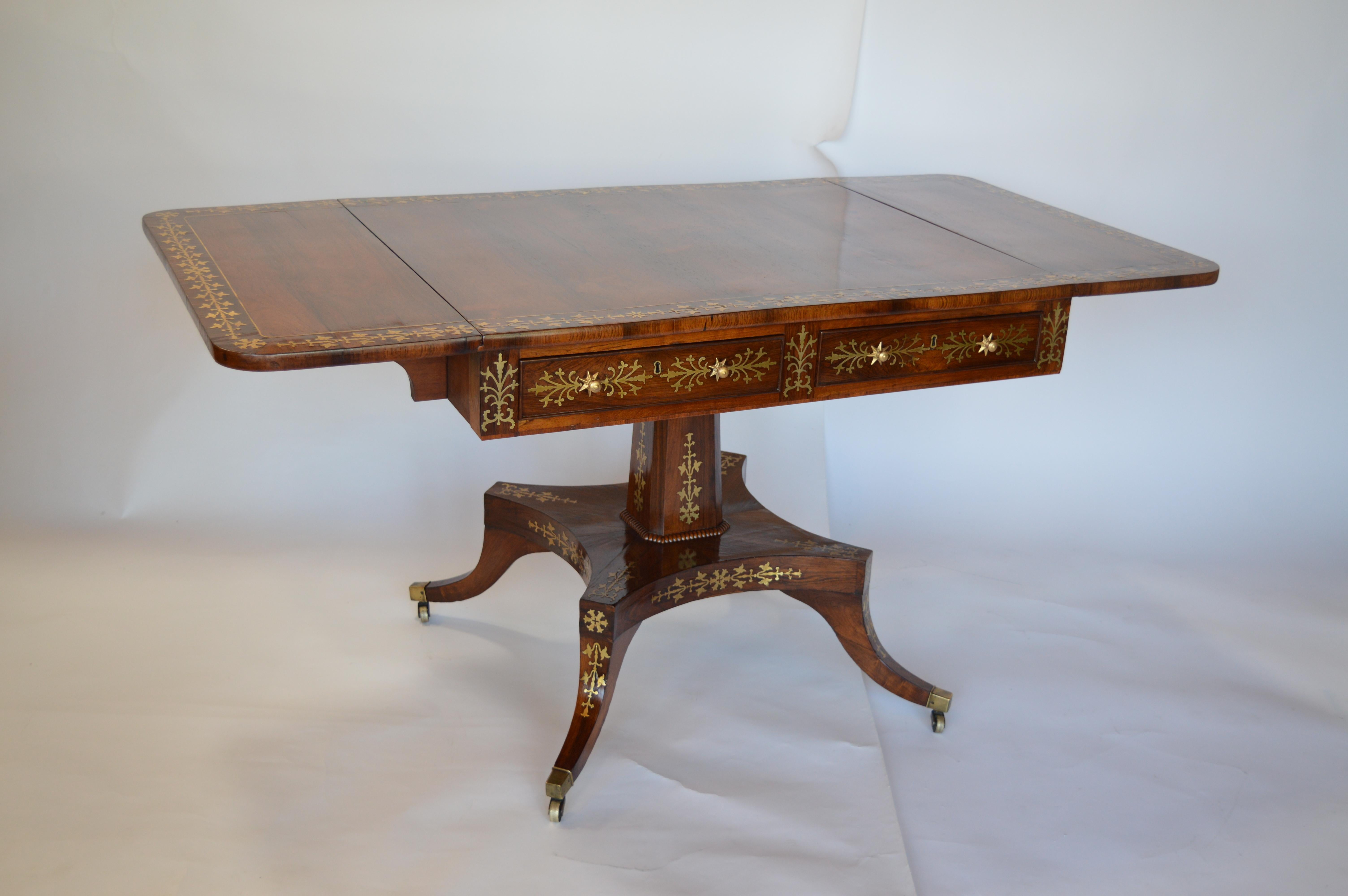 Regency rosewood pedestal table with brass inlaid and flowered details. Includes turned supports at the bottom of each leg.

