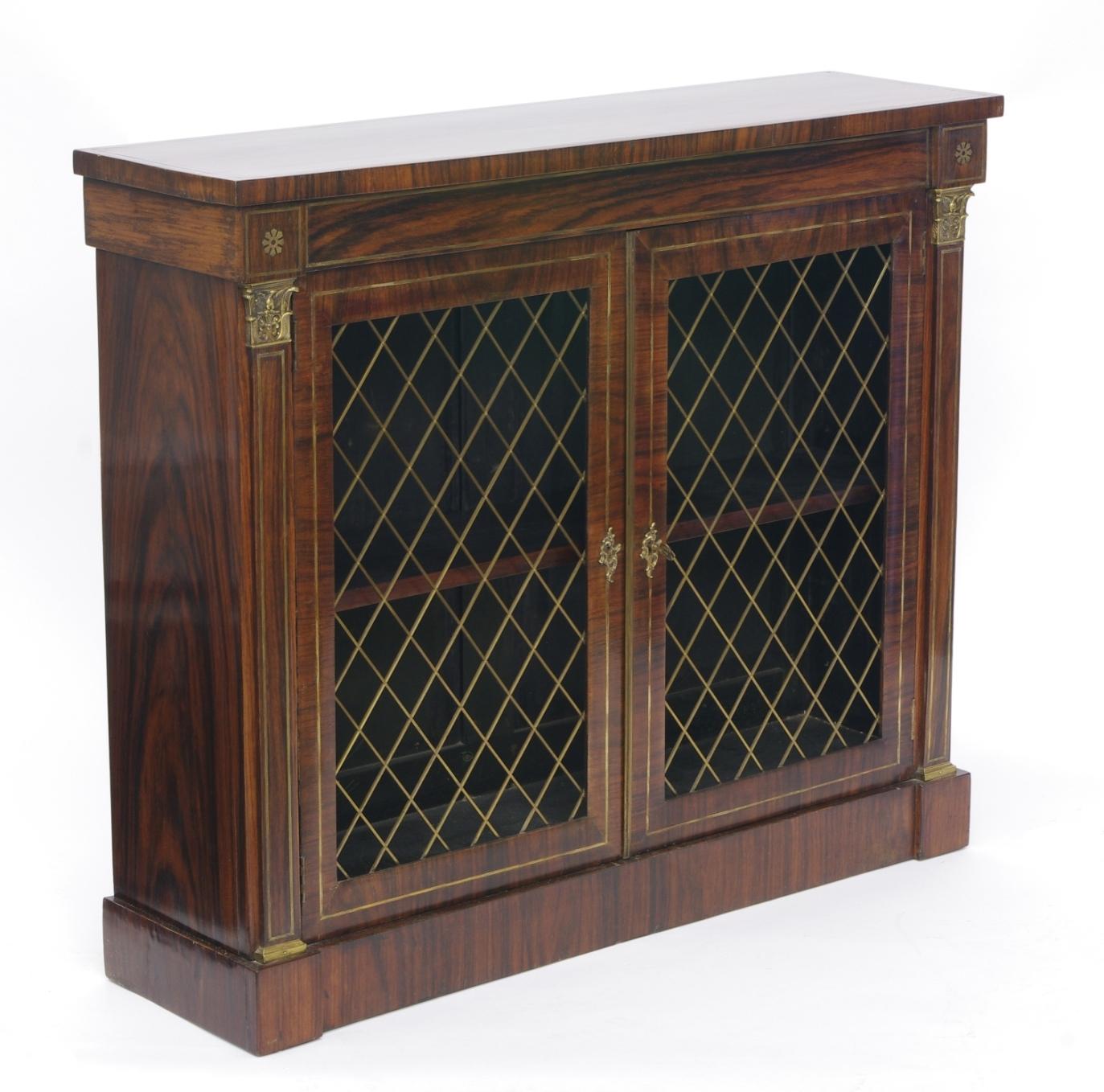 Regency rosewood bookcase side cabinet with overall brass inlay, the rectangular top over the narrow frieze with two flower bosses; the two doors with brass grill-work opening to a single adjustable shelf; the pilasters with Corinthian capitals