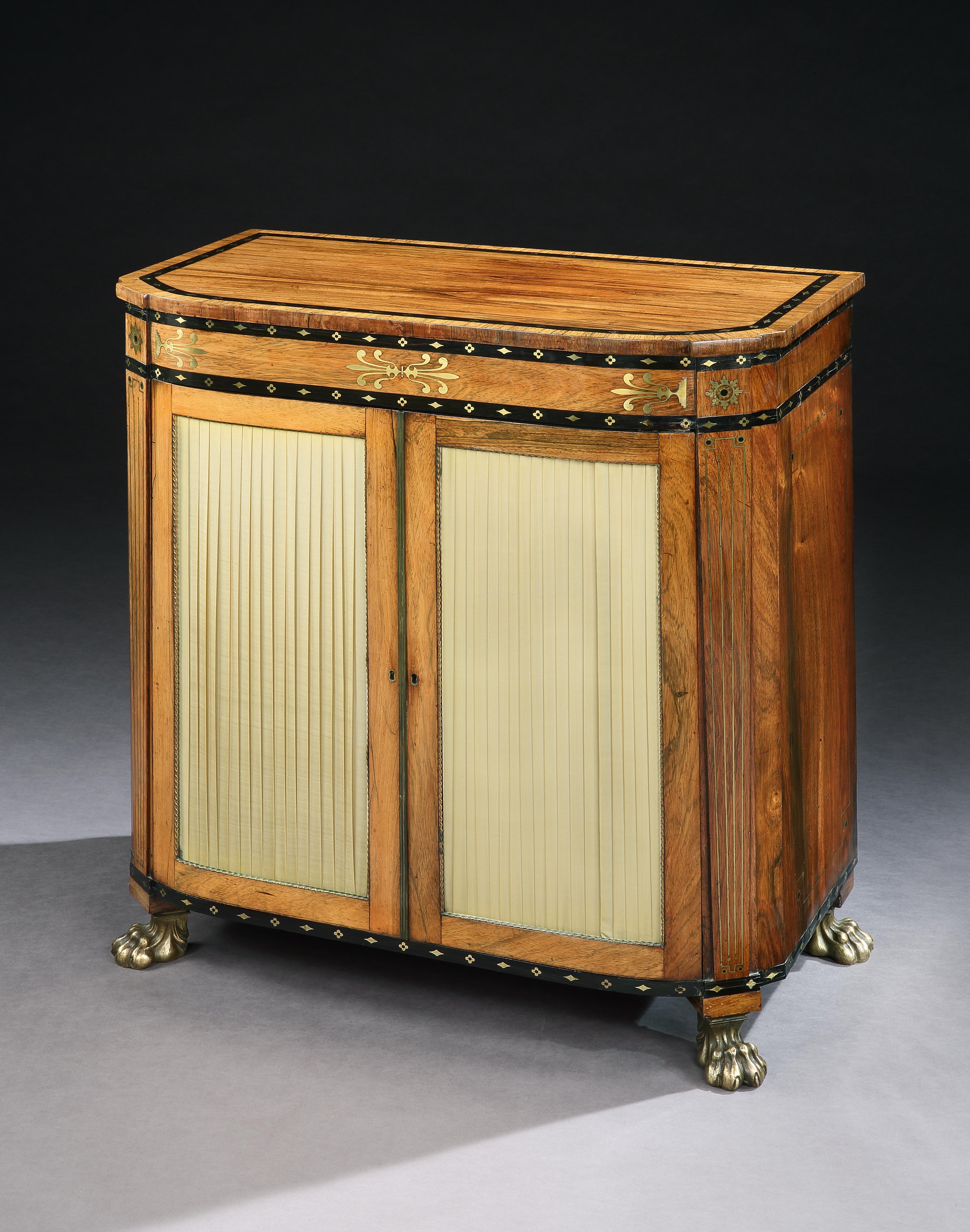 A elegant and quality Regency side cabinet in rosewood inlaid with brass and ebony inlay, the pleated panelled doors opening to reveal adjustable shelves, standing on brass paw castors.

 

English, circa 1810.

 

Provenance

Antique