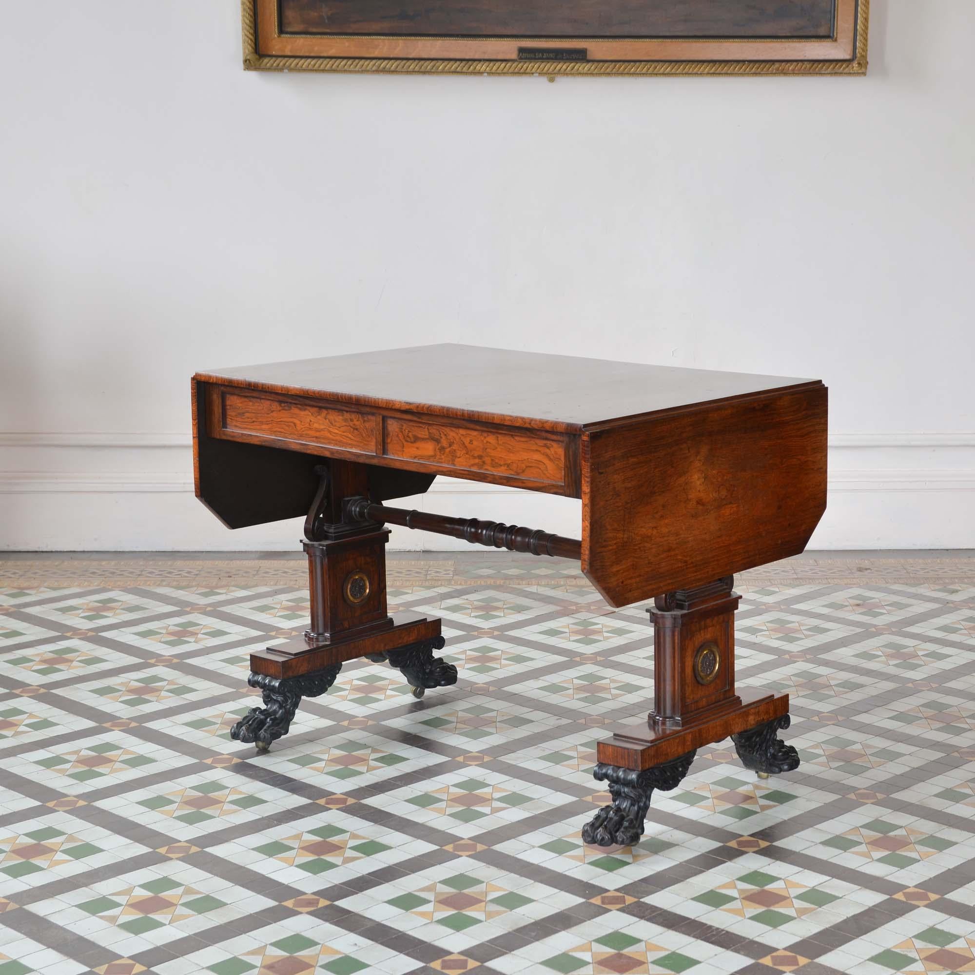 Regency rosewood sofa table by William Wilkinson. The well figured rectangular top, with folding leaves and canted corners, over a panelled frieze with a pair of concealed shallow drawers, with dummy drawers to the reverse. Supported by a pair of