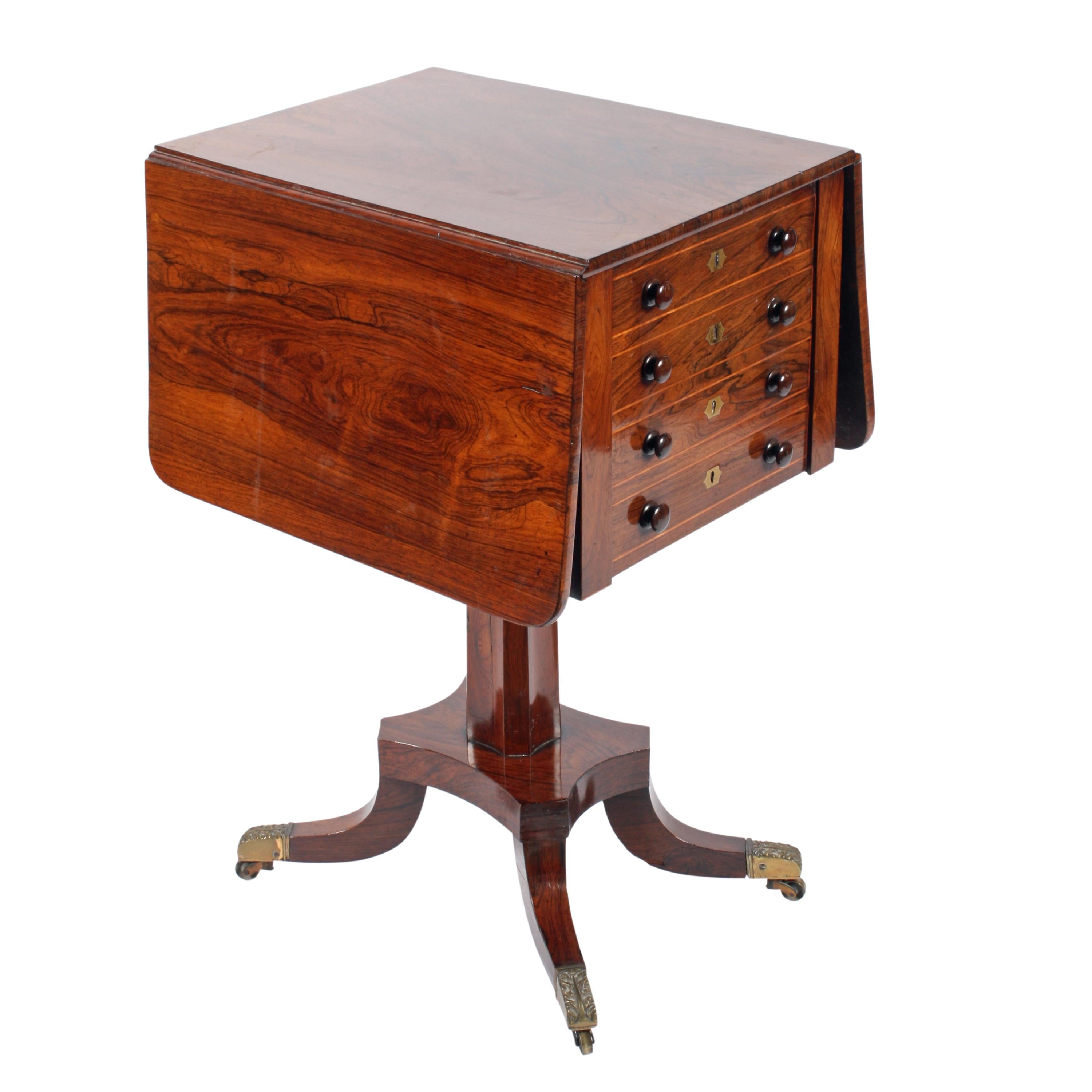 A Regency rosewood drop leaf work table.

The table stands on a platform base with four short sabre legs that have decorative brass toes and casters.

The tabletop has a triple drawer faced deep drawer with a fitted slim drawer above, all