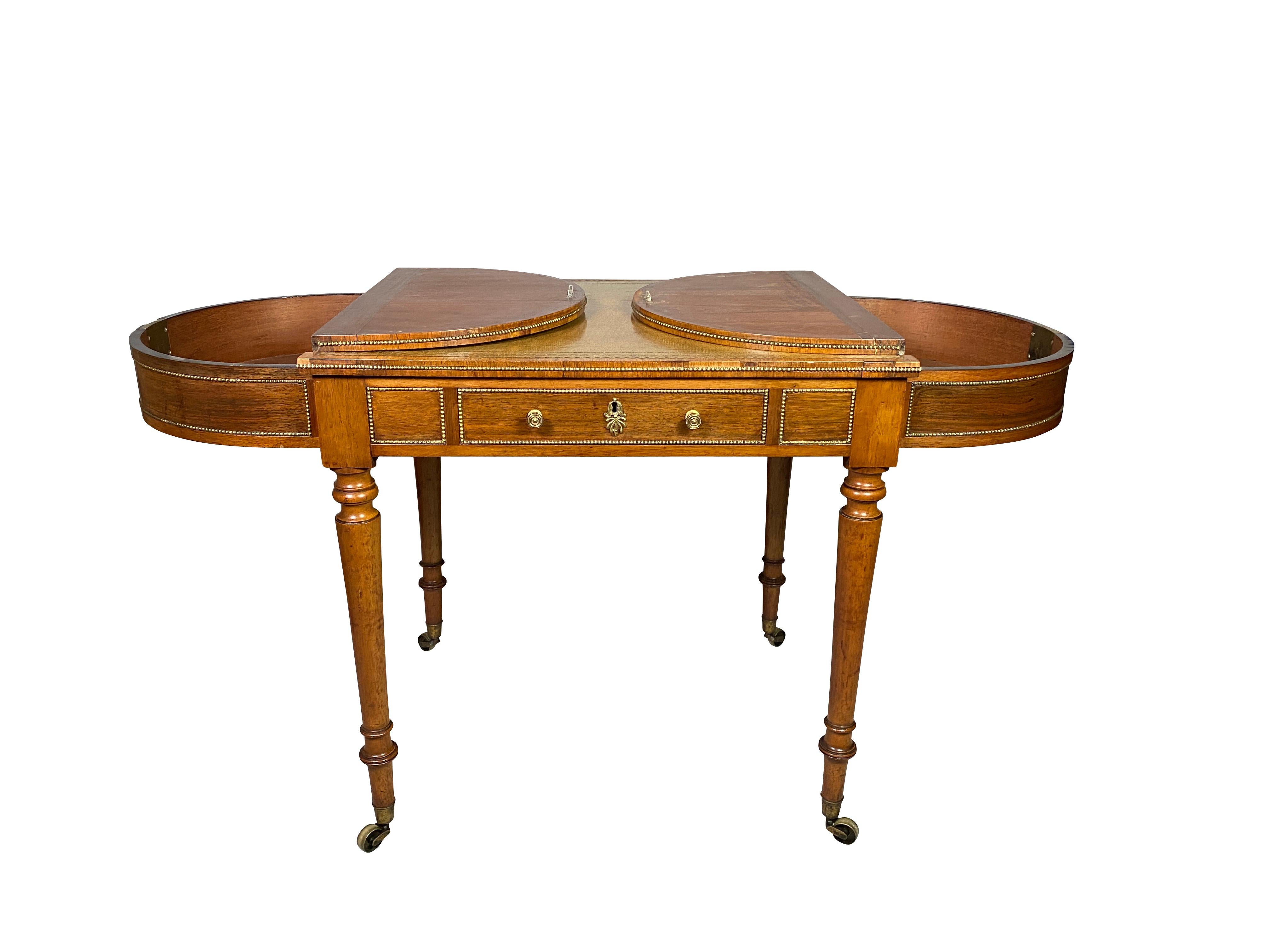 Most likely by Gillows. With rectangular beaded brass top with rounded ends with hinged lids , pale tooled green leather writing surface , conforming frieze with a drawer and the reverse with a false drawer raised on circular tapered legs ending on