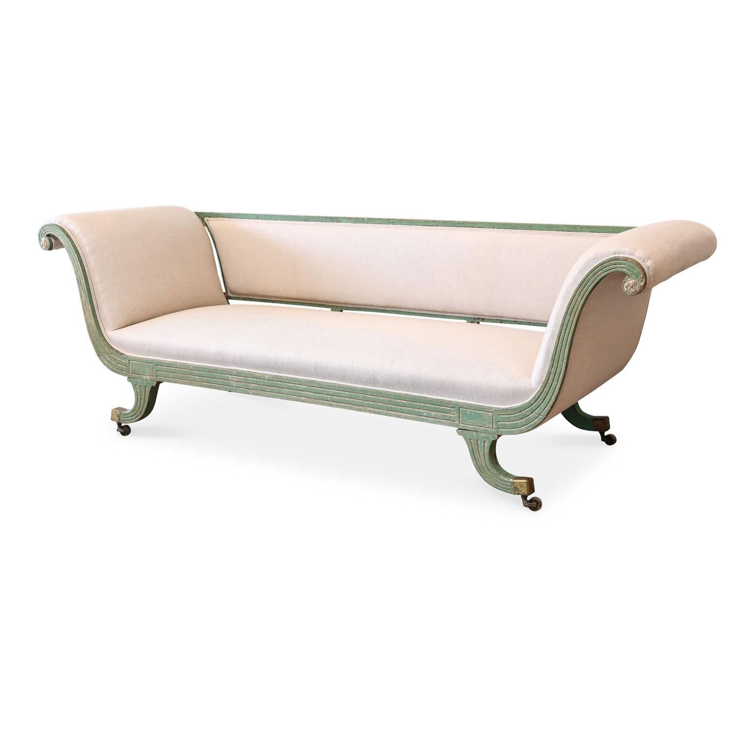 Regency scroll arm sofa constructed, circa 1820 for an English country estate. Stands upon out swept legs (supported by original gilt brass castors). Sofa is dry-scraped back to its original green paint with traces of gilt. Carved decorative