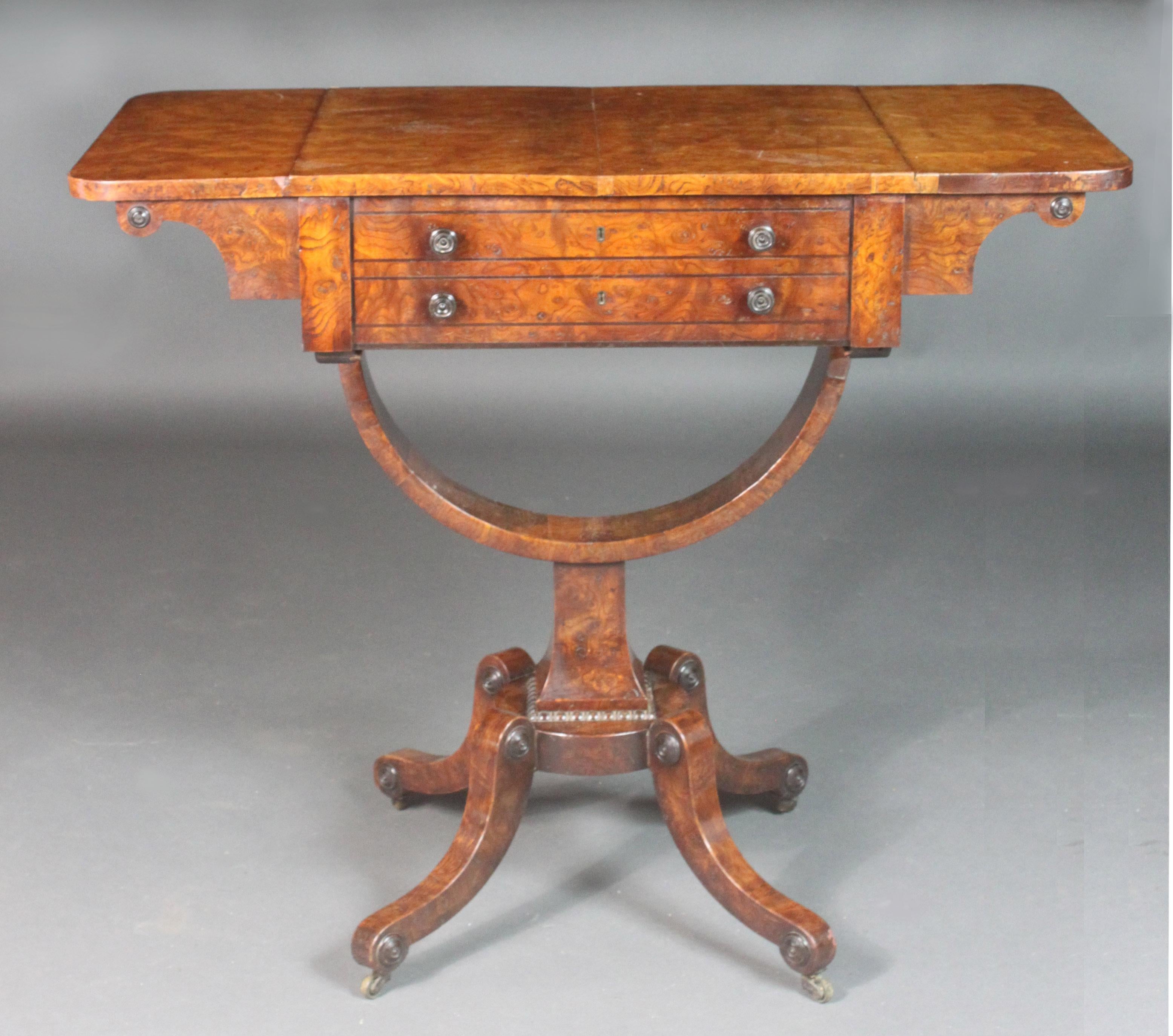 Regency sewing table in the very attractive wood, burr ash, with ebony stringing, knobs and paterae. Good original colour and patina. When open, the flaps supported by veneered lopers with more applied paterae. The base with bobbin-turned mouldings,