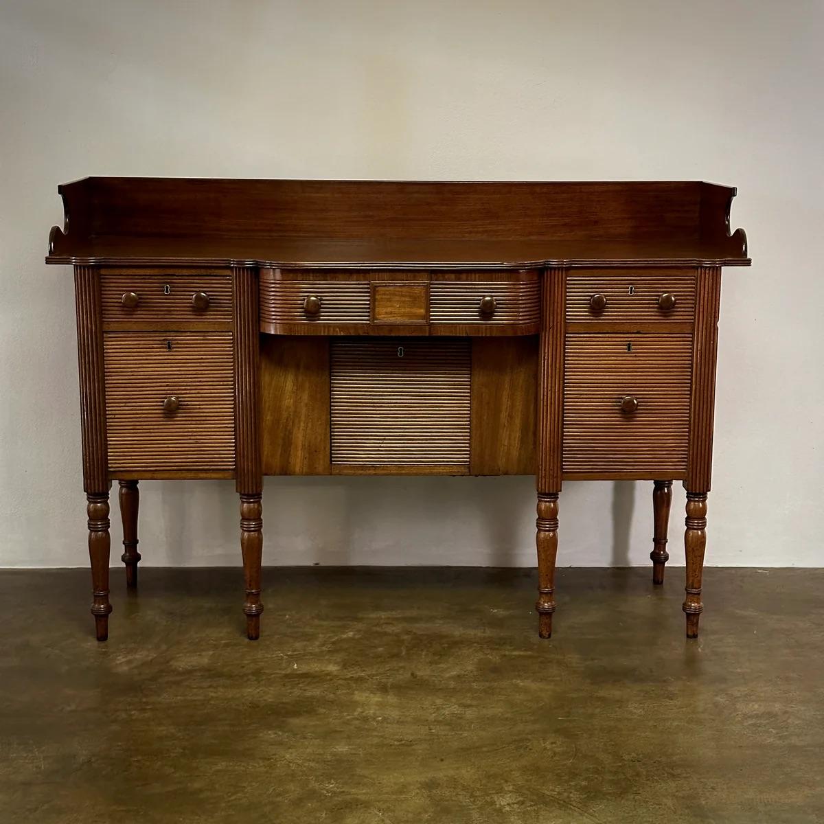 Credenza Regency in mogano, proveniente dall'Irlanda. Questo pezzo di classe presenta una disposizione equilibrata delle opzioni di archiviazione con ante a coste e cassetti scorrevoli, il tutto su gambe delicatamente tornite. Gli intricati elementi