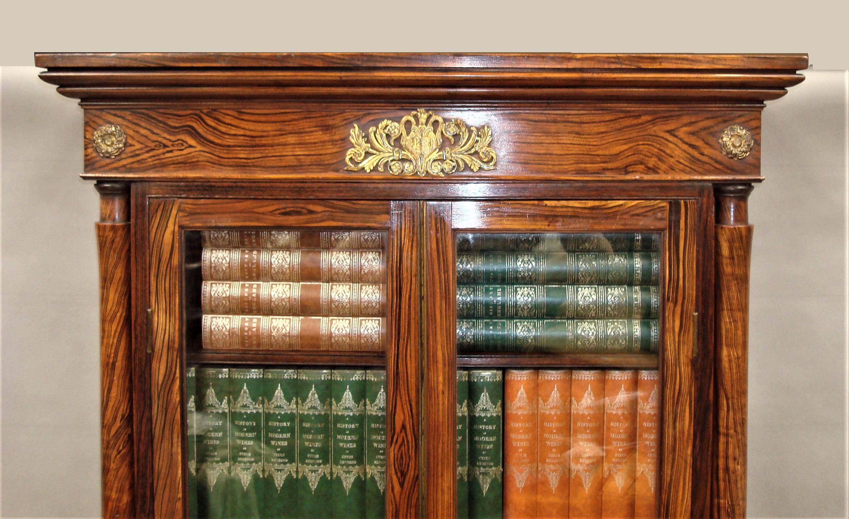 A good Regency simulated faux calamander bookcase of small proportions with unusual original painted finish; the moulded cornice with a central gilt bronze classical mount with rosettes to either side above a pair of long glazed doors flanked by