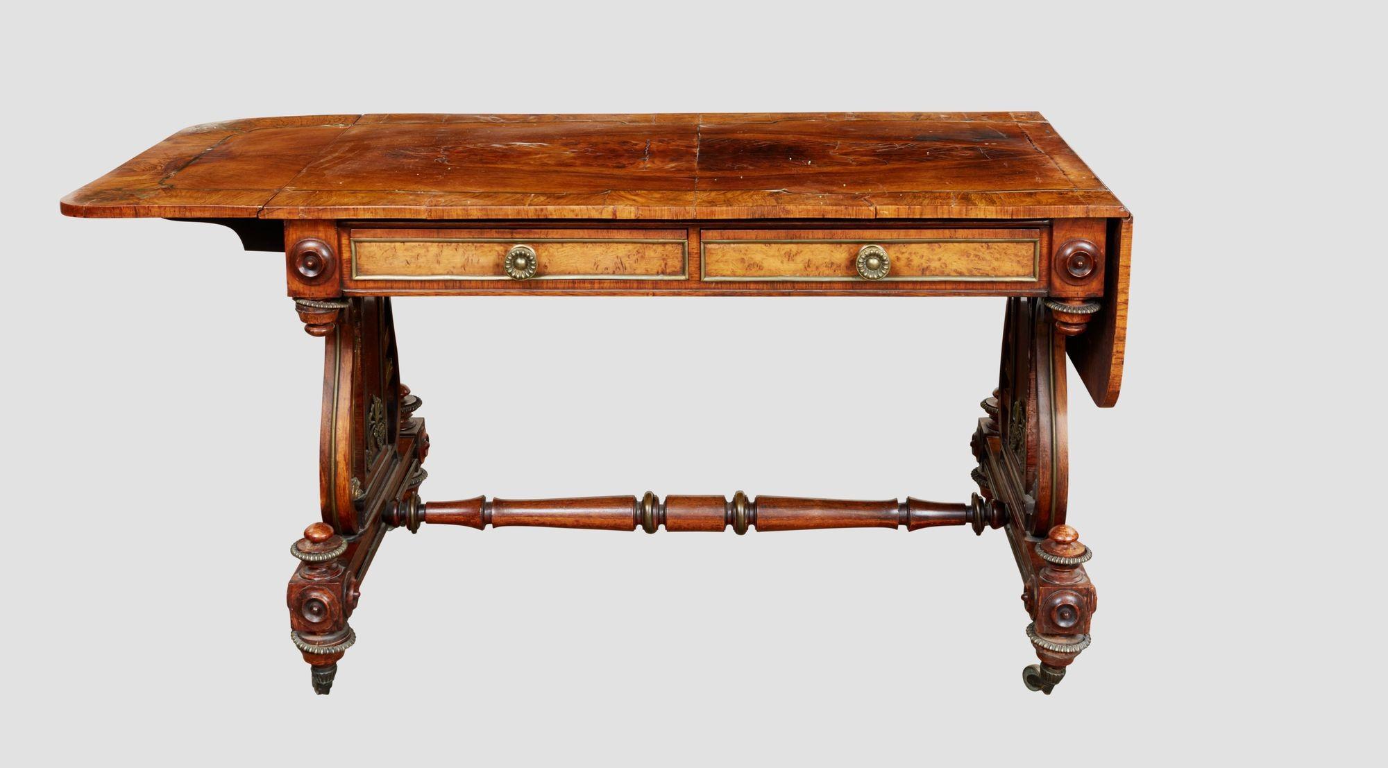A spectacular sofa table in the manner of George Bullock with intimations of designs by Thomas Hope having a rosewood veneered top banded in oak with brass inlaid florets at the corners with two drawers with unusual trestle supports with brass