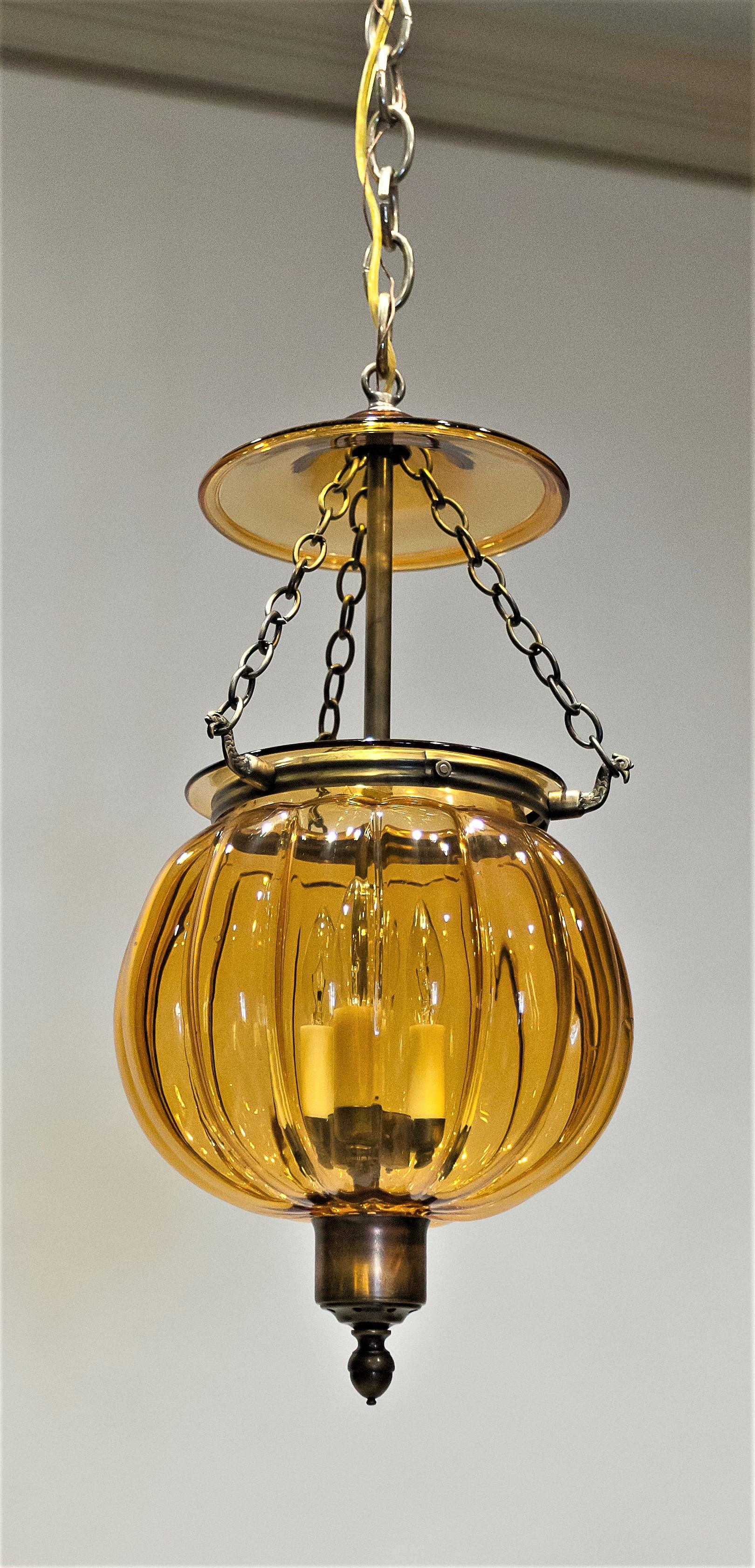Hand blown amber glass in a pumpkin shape. Reproduction of a design popular in the 1830's and 1840's as a candle-burning fixture. Hand cast aged brass. Electrified with a three-light cluster that gives a wonderful warm glow through the amber glass.