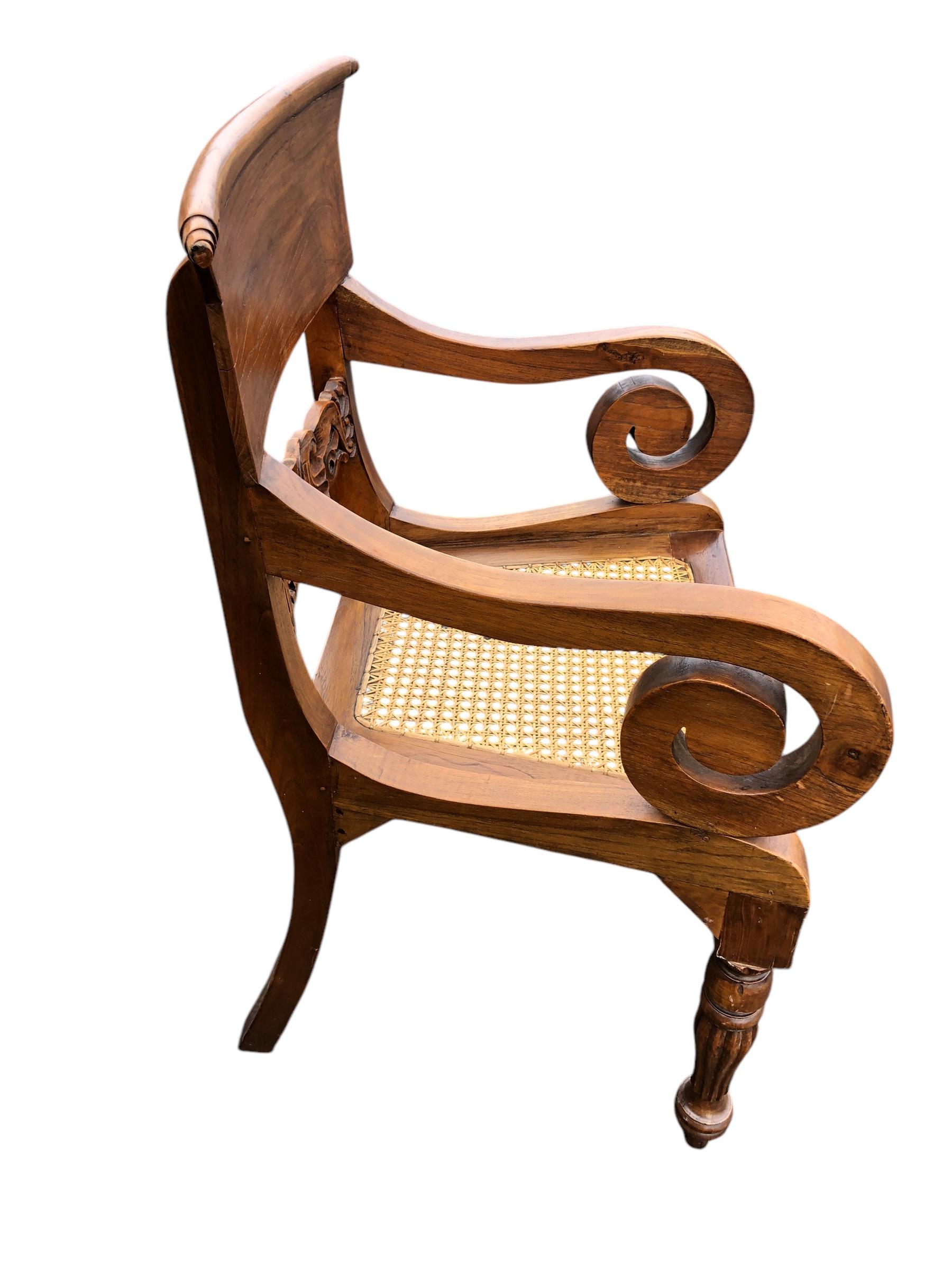 Fauteuil anglo-indien bien proportionné.  Sculptée à la main dans du bois de rose, la chaise est ornée de rosettes et le dossier est sculpté en forme de cornes. L'assise est en rotin tressé et est généralement munie d'un coussin non fixé.
Veuillez