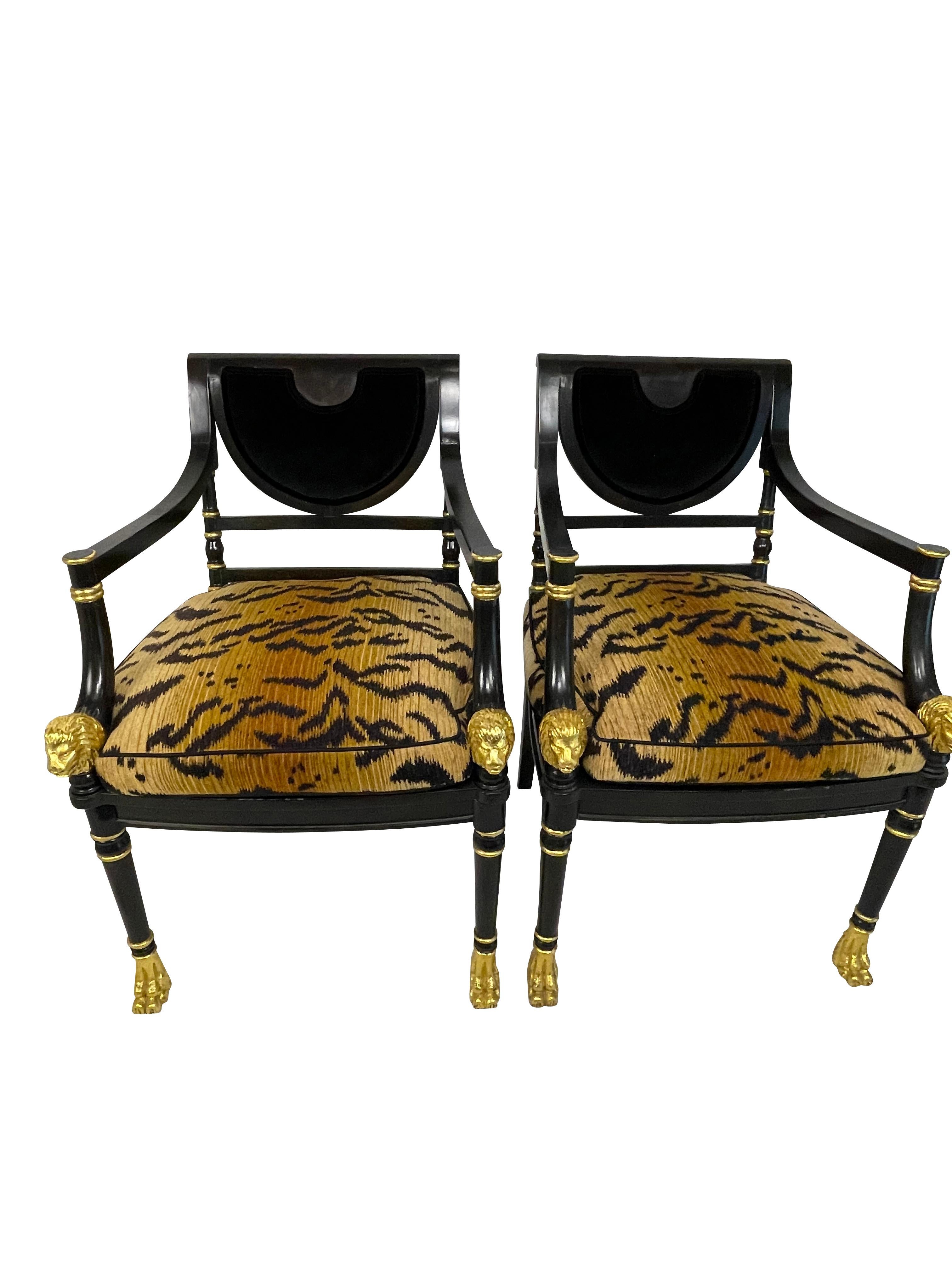 Two carved Regency style ebonized and gilt decorated chairs with carved gilt lion heads and feet, animal print fabric cushions over cane seats, and velvet backs. 35.75