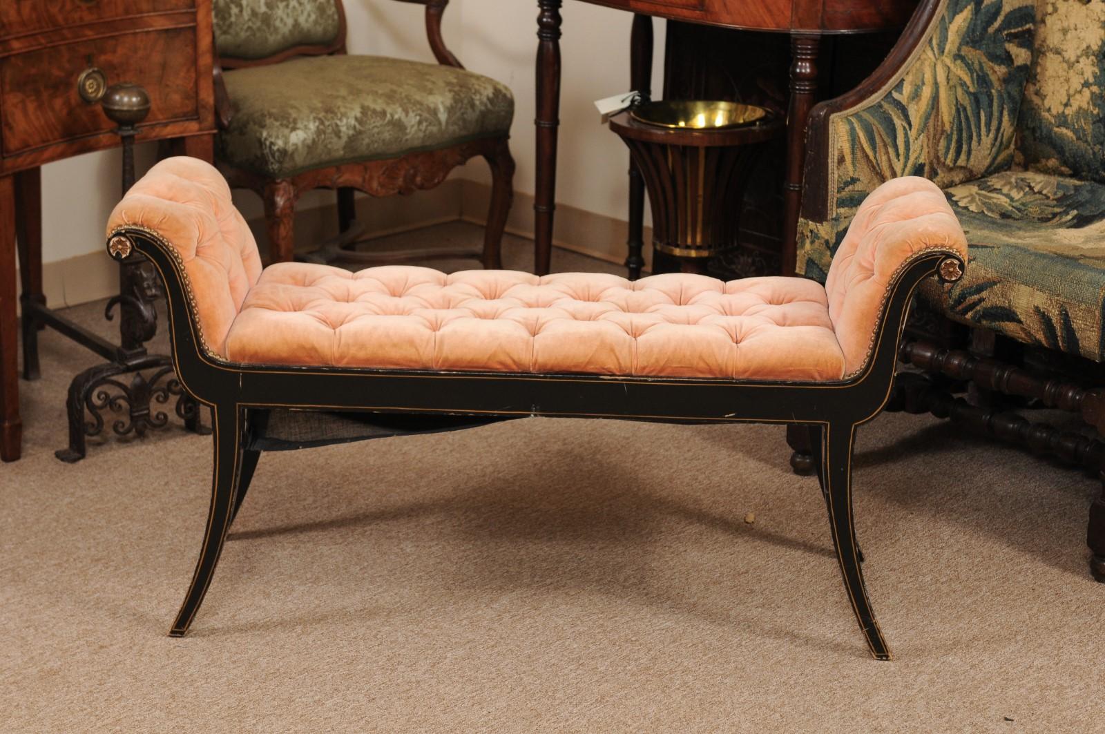 The Regency style black painted and parcel-gilt bench with scrolled arms with carved flower detail, velvet tufted upholstery in peach hues and all resting on splayed legs. 

  