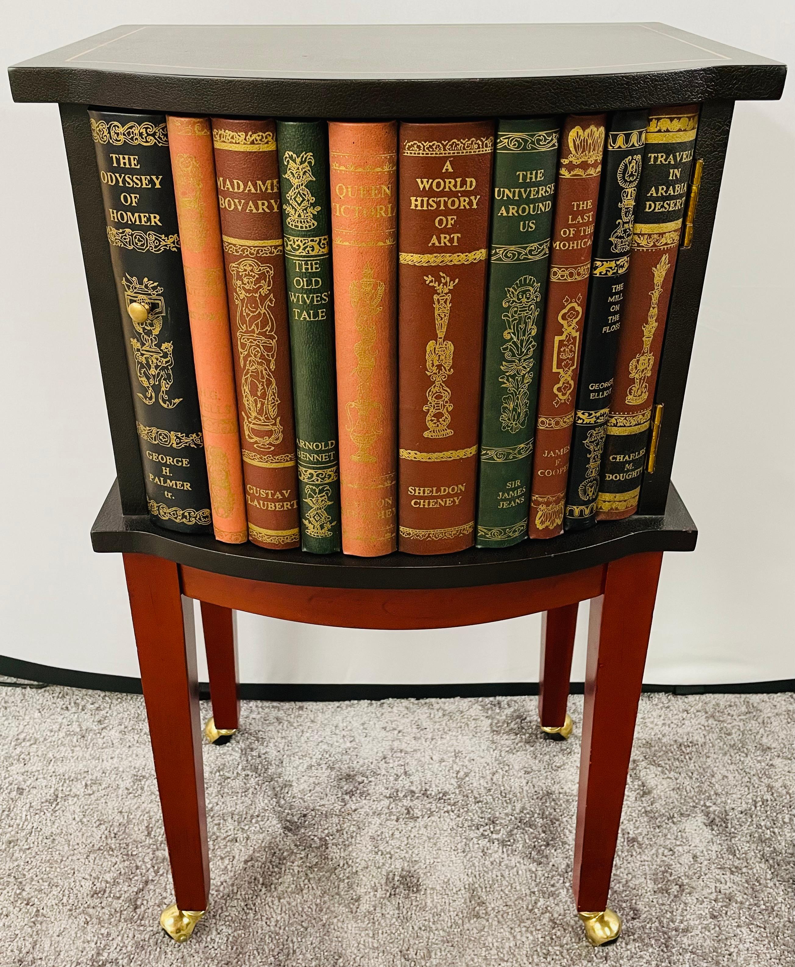 A lovely Regency style night stand or end table featuring a black tooled leather top decorated with a gold line and one door cabinet. The cabinet door is hand painted to display a splendid design of rare and collectible books. The table is raised on