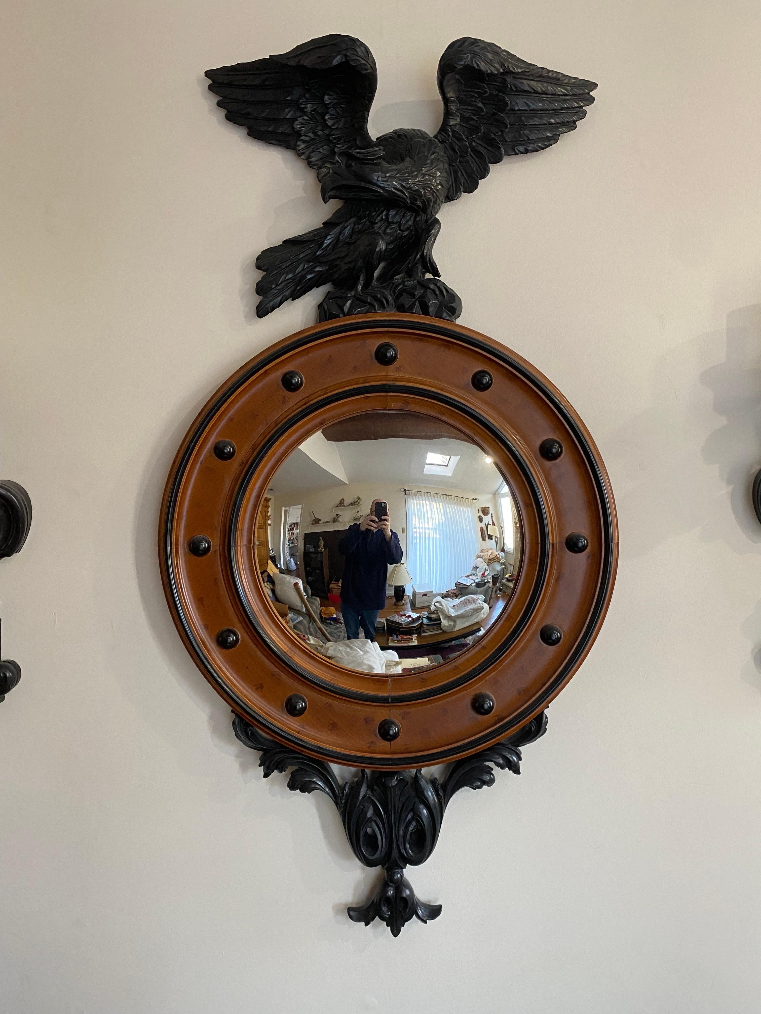 Un grand miroir de style Regency avec un cadre rond en érable à œil d'oiseau et un miroir central en verre bombé. Il est surmonté d'un grand aigle en résine noire coulée à la main et rehaussé d'un ornement en volutes assorti. Le poids est