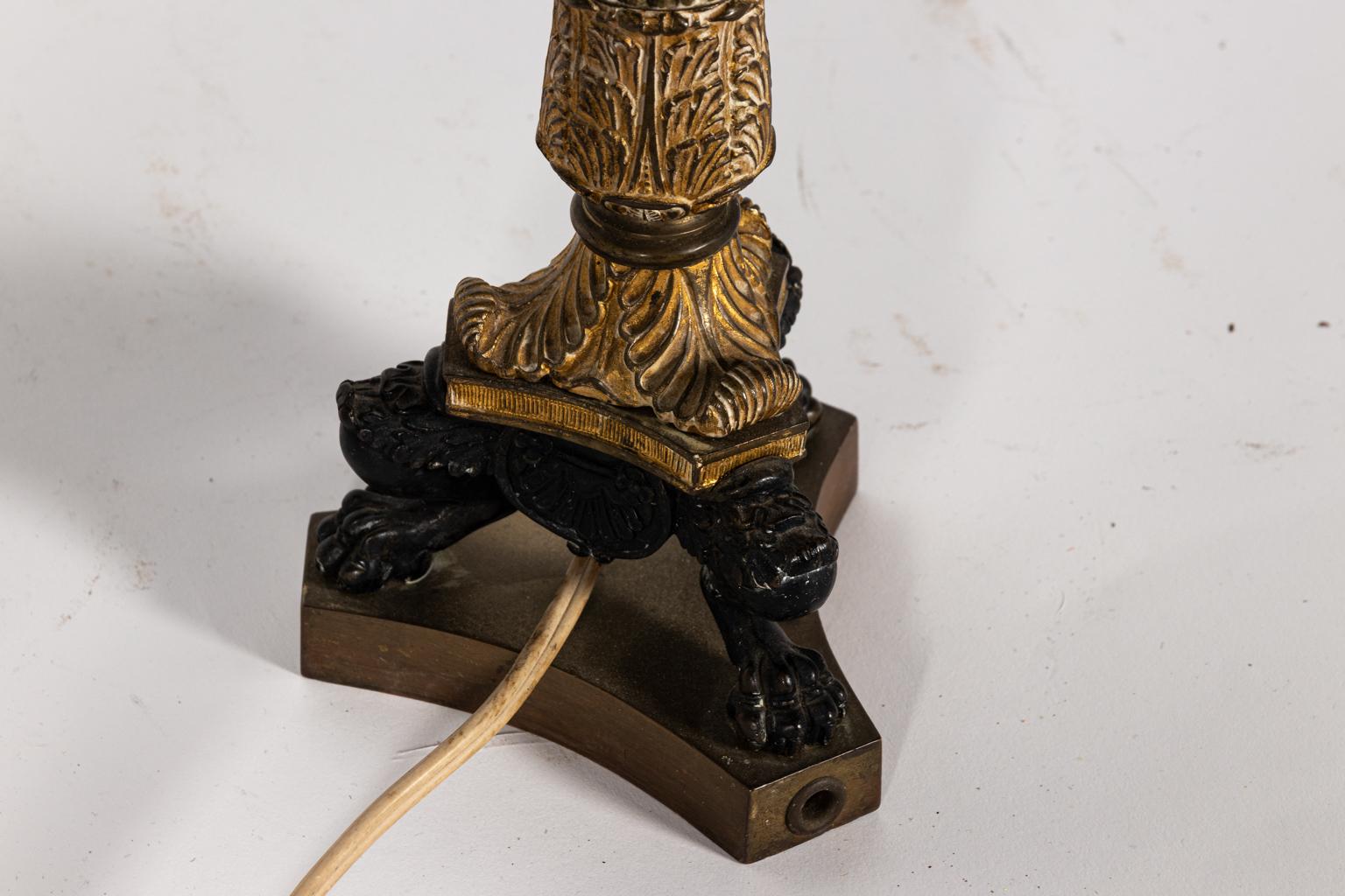 Regency style candlestick lamp with tole shade. The piece also features a fluted column base with foliage and lion's paw feet. Please note of wear consistent with age including chips and minor finish loss. Shade not included.