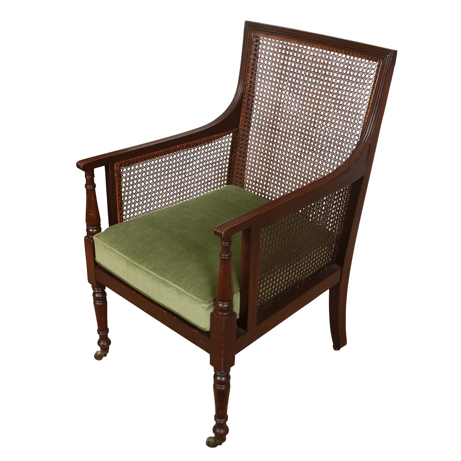 A vintage stately Regency style caned chair with straight frame caned sides and back with reeded arms and turned legs that continue to the arm rests and end on casters at the base. The chair seat is newly upholstered with a mossy green velvet, box