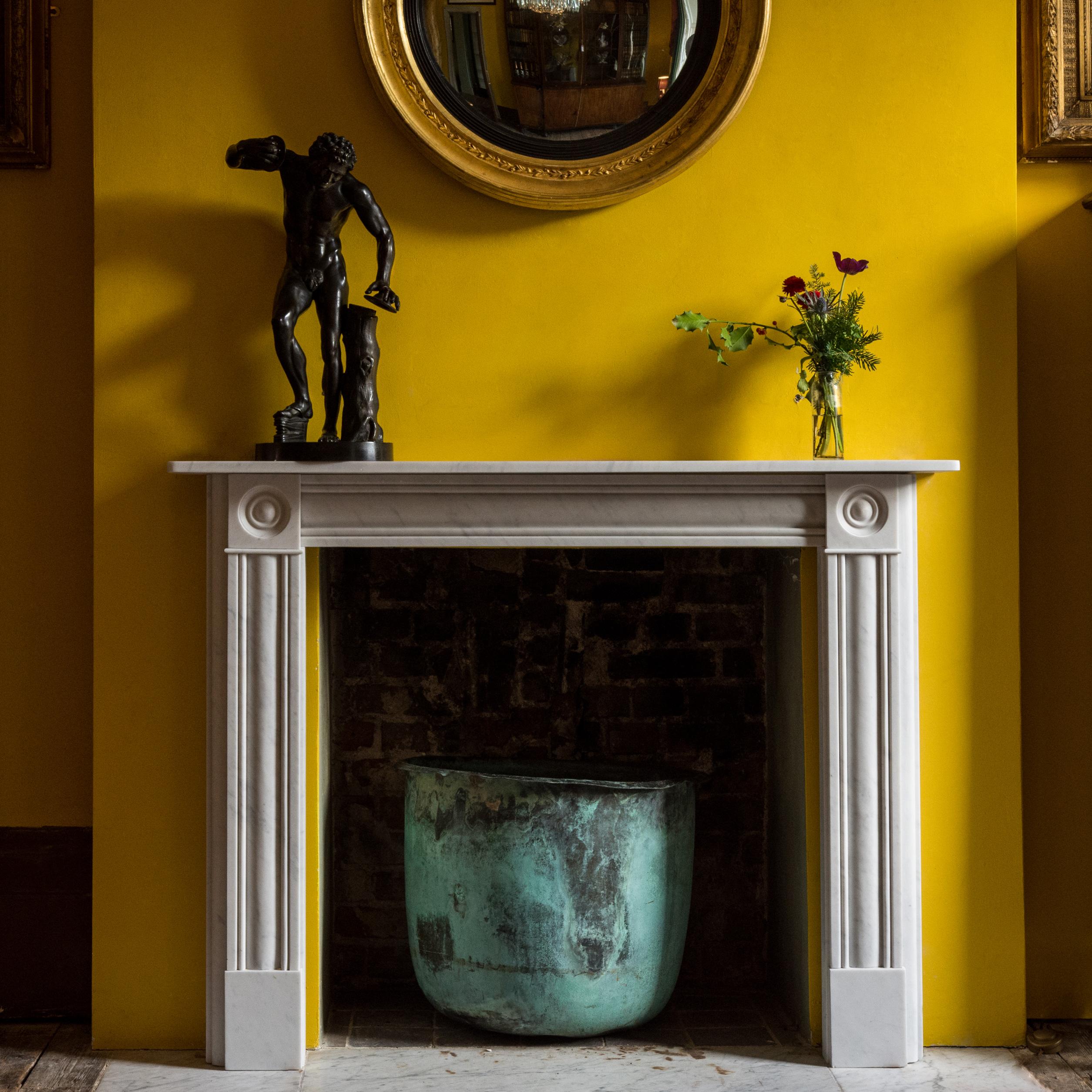 A Regency style Carrara marble bullseye fireplace, the rectangular shelf above cushion molded frieze flanked by bullseye roundels, the conforming jambs on square footblocks. Measures: Aperture: height 91cm, width 91cm.