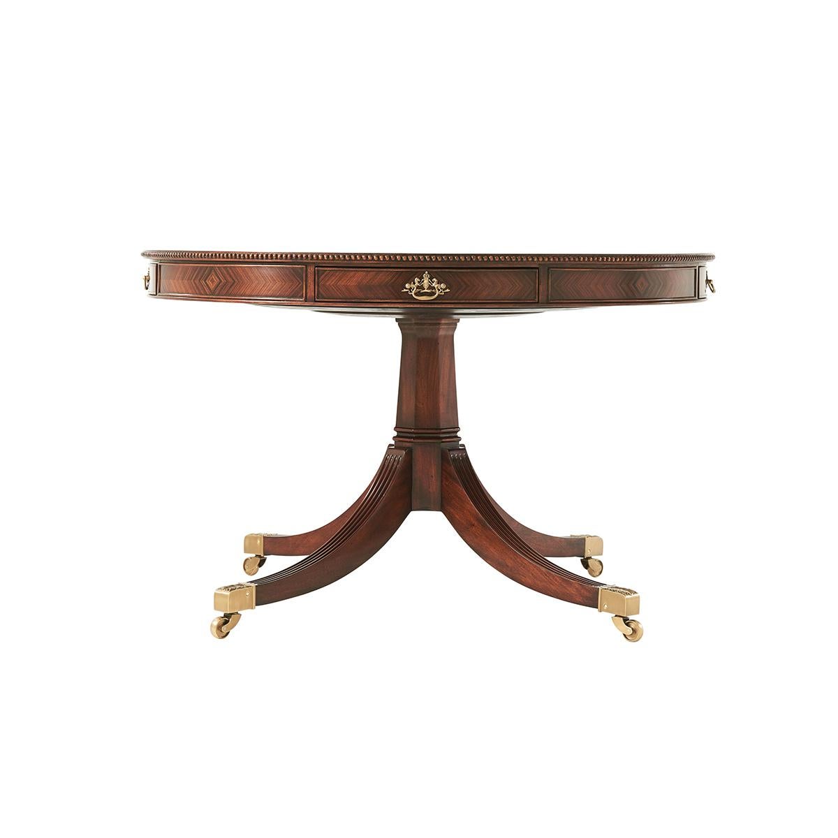 A Regency style morado and pollard banded circular center table, with a carved edge and four frieze drawers with brass handles, the hexagonal column issuing outswept reeded legs on castors. At 30