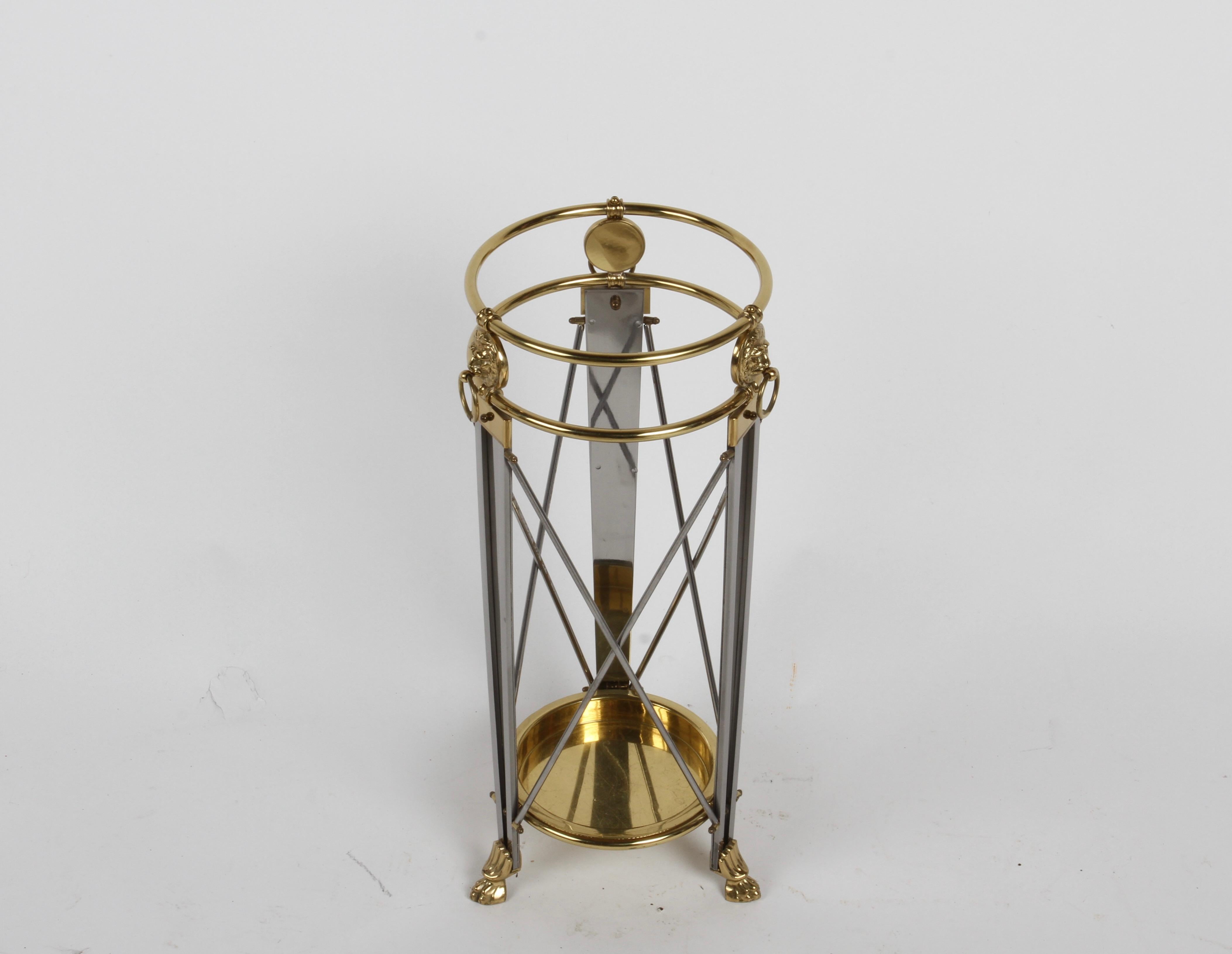 Hollywood Regency or Empire style classic form umbrella stand in stainless steel & brass with brass lions heads with ring, on stainless legs with brass paw feet and stainless X stretchers. Brass tray at the bottom, has minor scuffs and a few dings. 