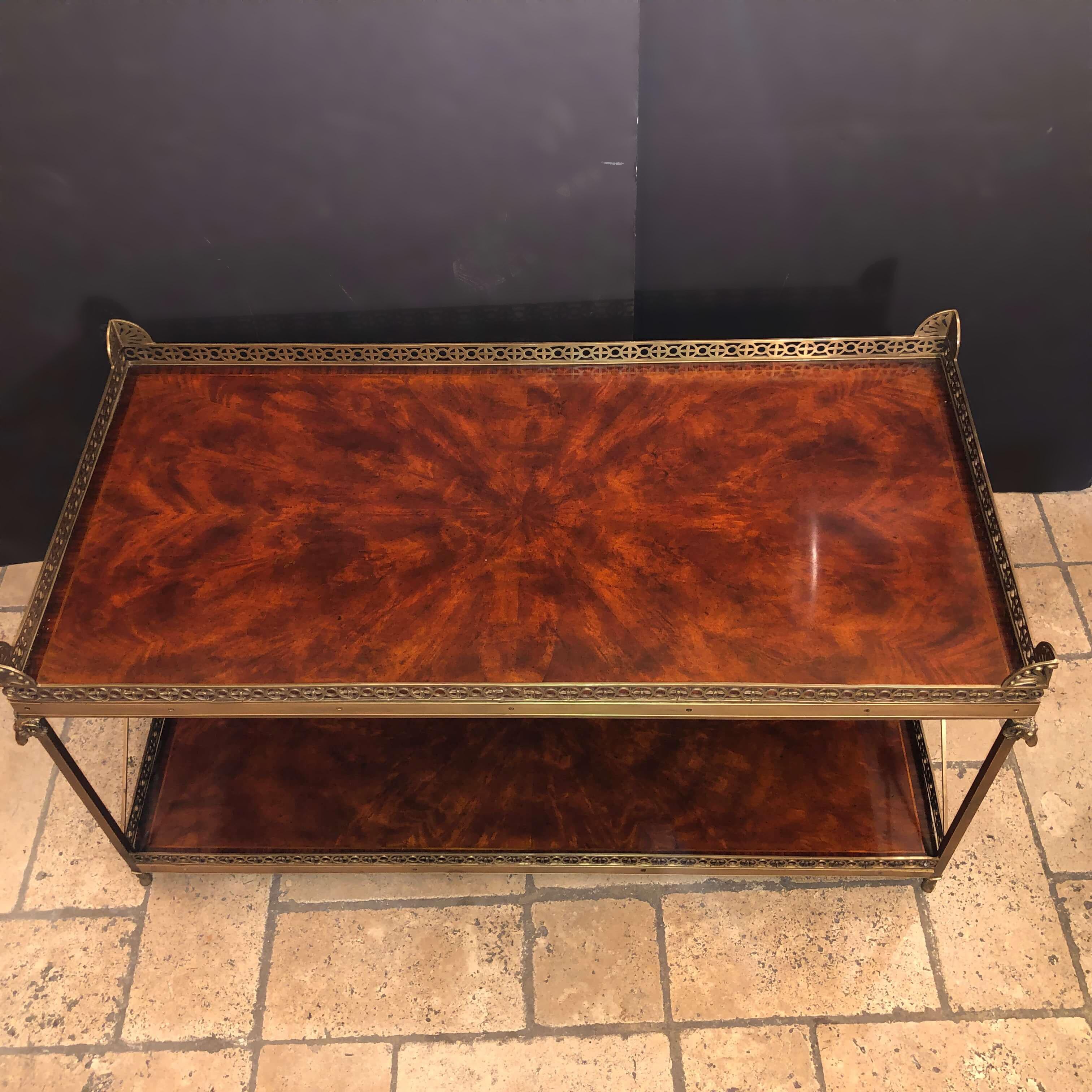 Regency style two-tier mahogany and brass coffee table with Ram's head mounts, X-frame supports, figured mahogany shelves, pierced brass galleries, and palmettes, raised on hoof feet.