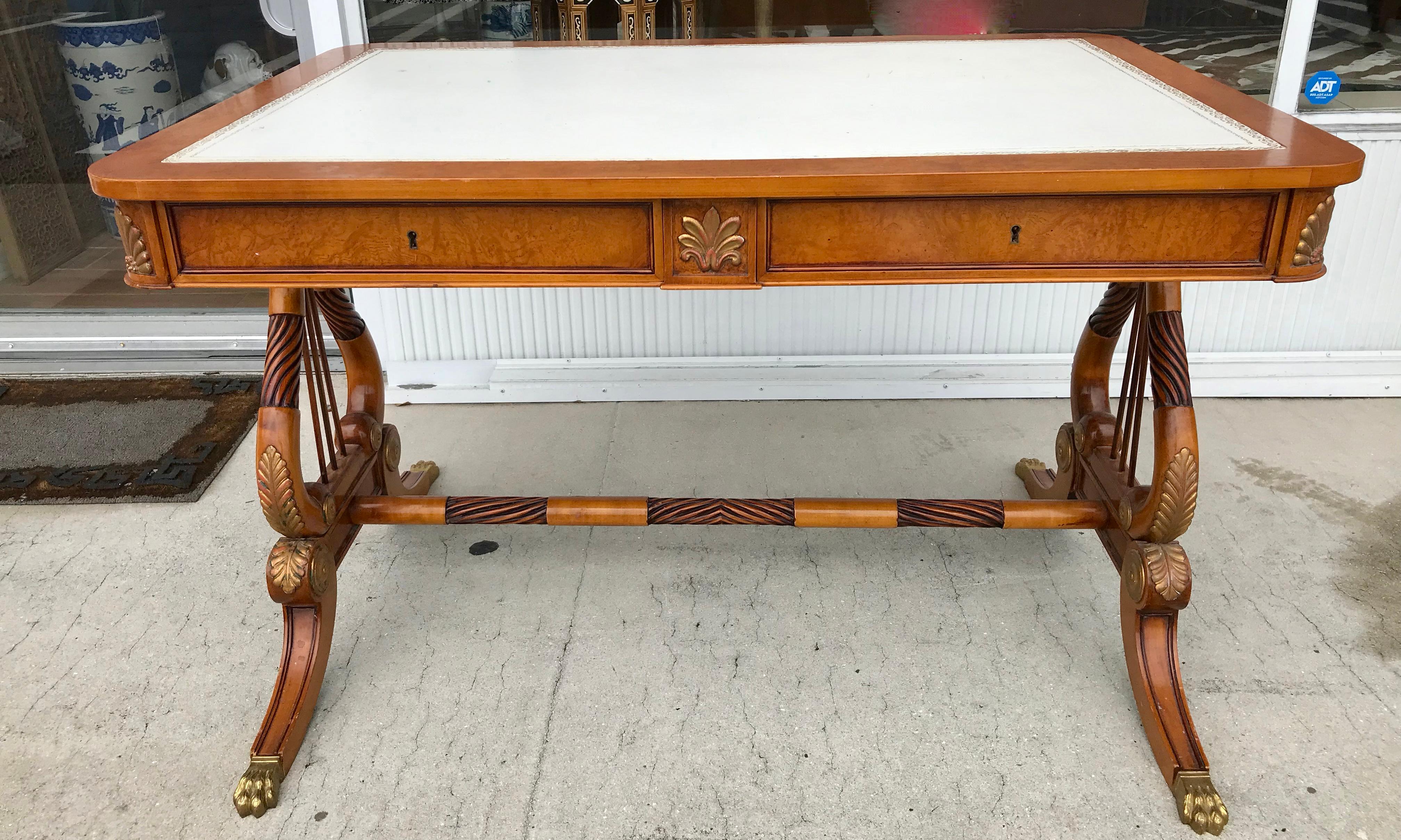 The desk is fitted with a gold embossed white leather top.
The ends are lyre form. The fruitwood is embellished with gilt accents.
The piece is fitted with 2 drawers and terminating with brass lion paw feet.