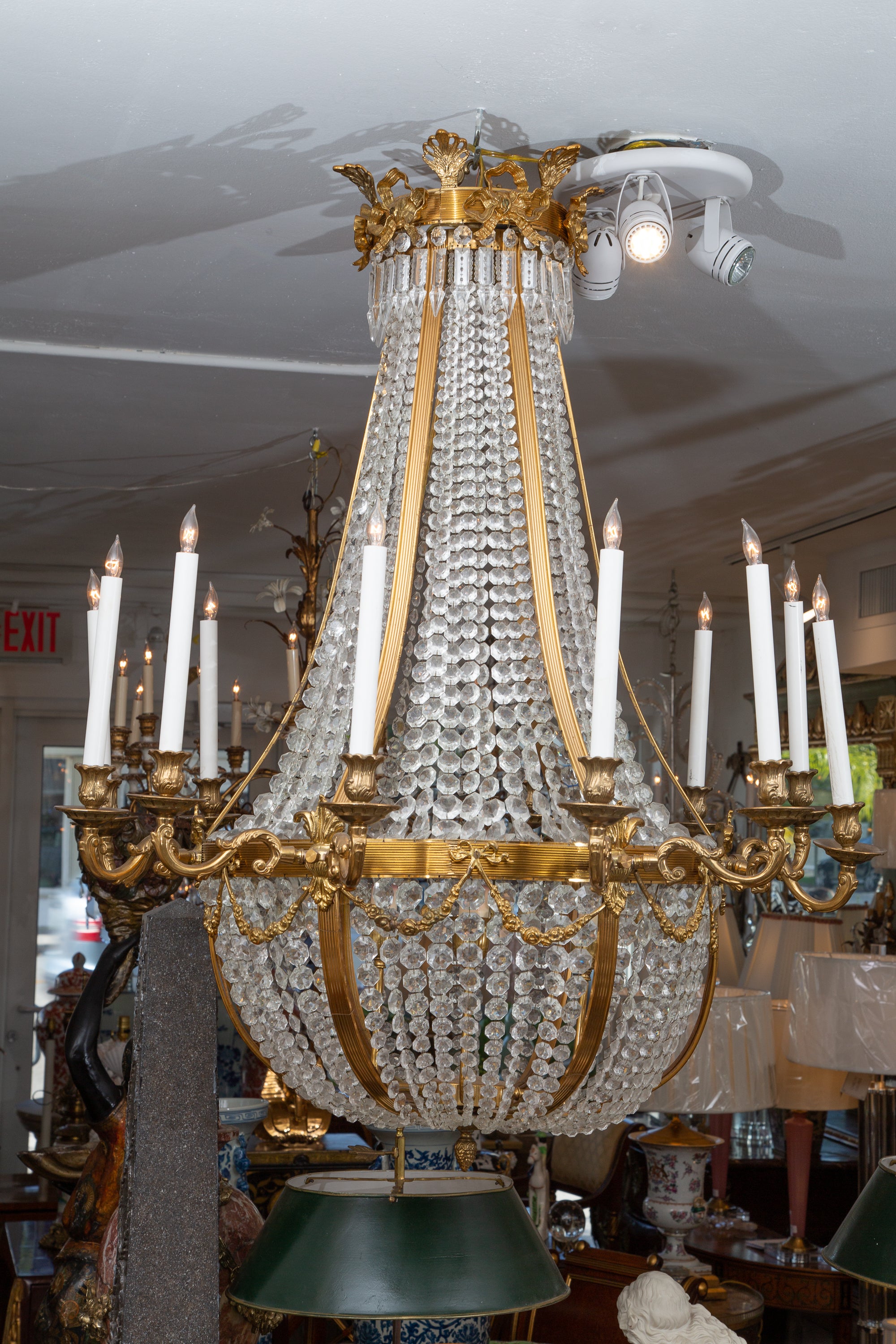 This is a classic French Regency style 12-light chandelier with faceted crystal strands cascading in waterfall fashion within a gilt metal frame. The entire structure is enhanced by bows and swags. Three additional lights on arms in the center
