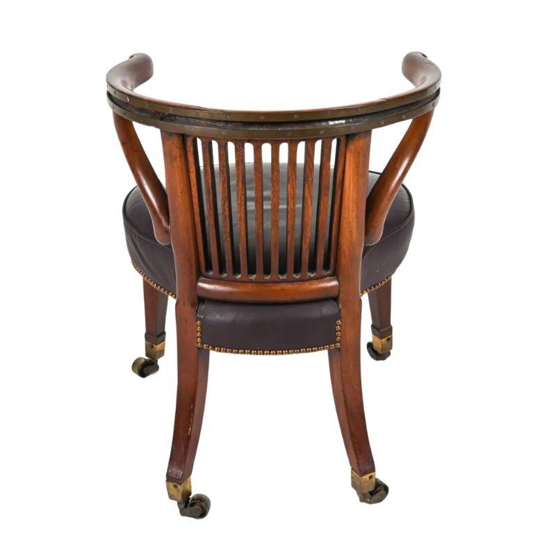 Chaise de bureau de style Regency vintage avec assise ronde en cuir, pieds à roulettes avec capuchons en laiton, dossier à lattes droites et supports décoratifs courbés de chaque côté.  