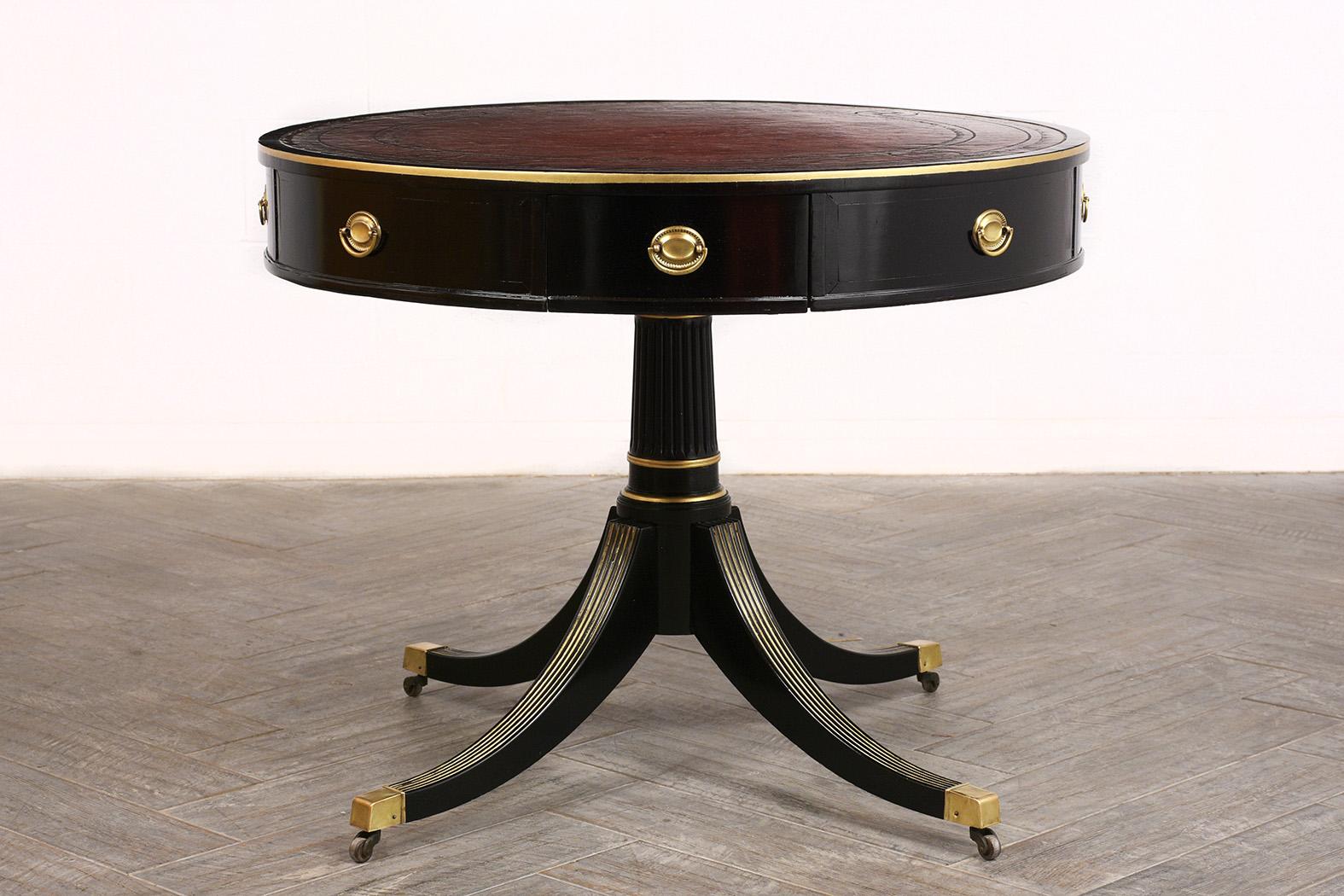 This early 1900s antique Regency-style center table comes with the original embossed leather top dyed in a dark redish-brown color with beautiful distressed details, ebonized finish, four faux drawers and two actual drawers with brass pull handles.