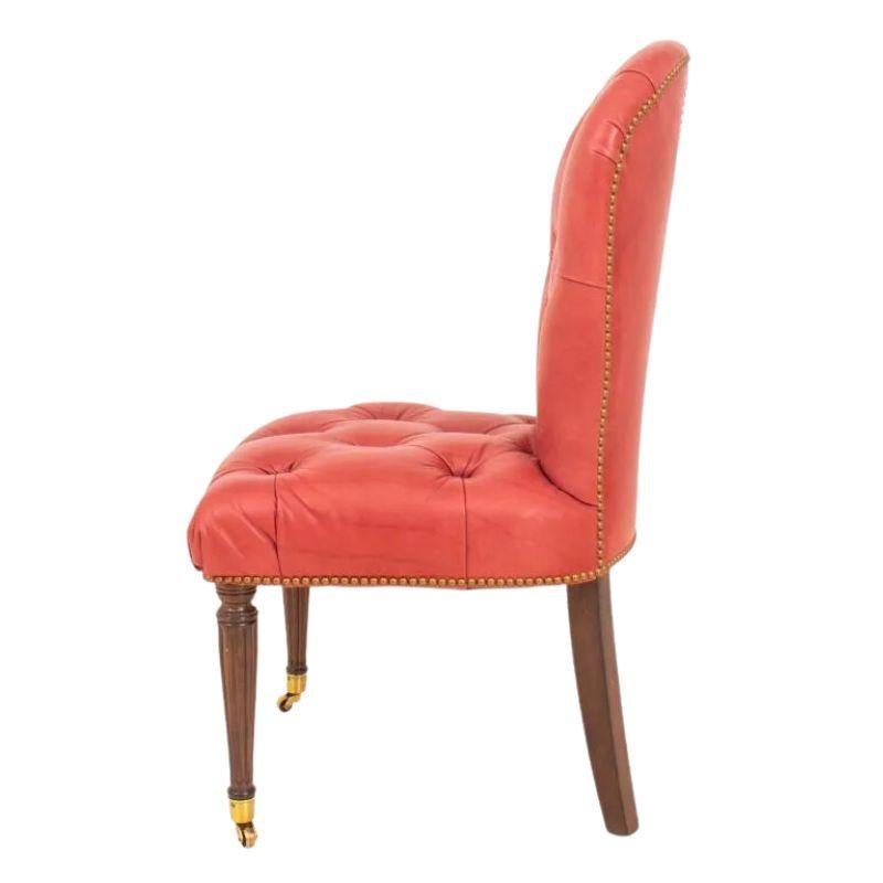 A Regency style, red leather tufted upholstered side chair with mahogany legs from Edward Ferrell. The chair has a shaped back, nail head trim, straight tapered and fluted front legs ending on casters and rear legs are sabre shaped. Circular detail