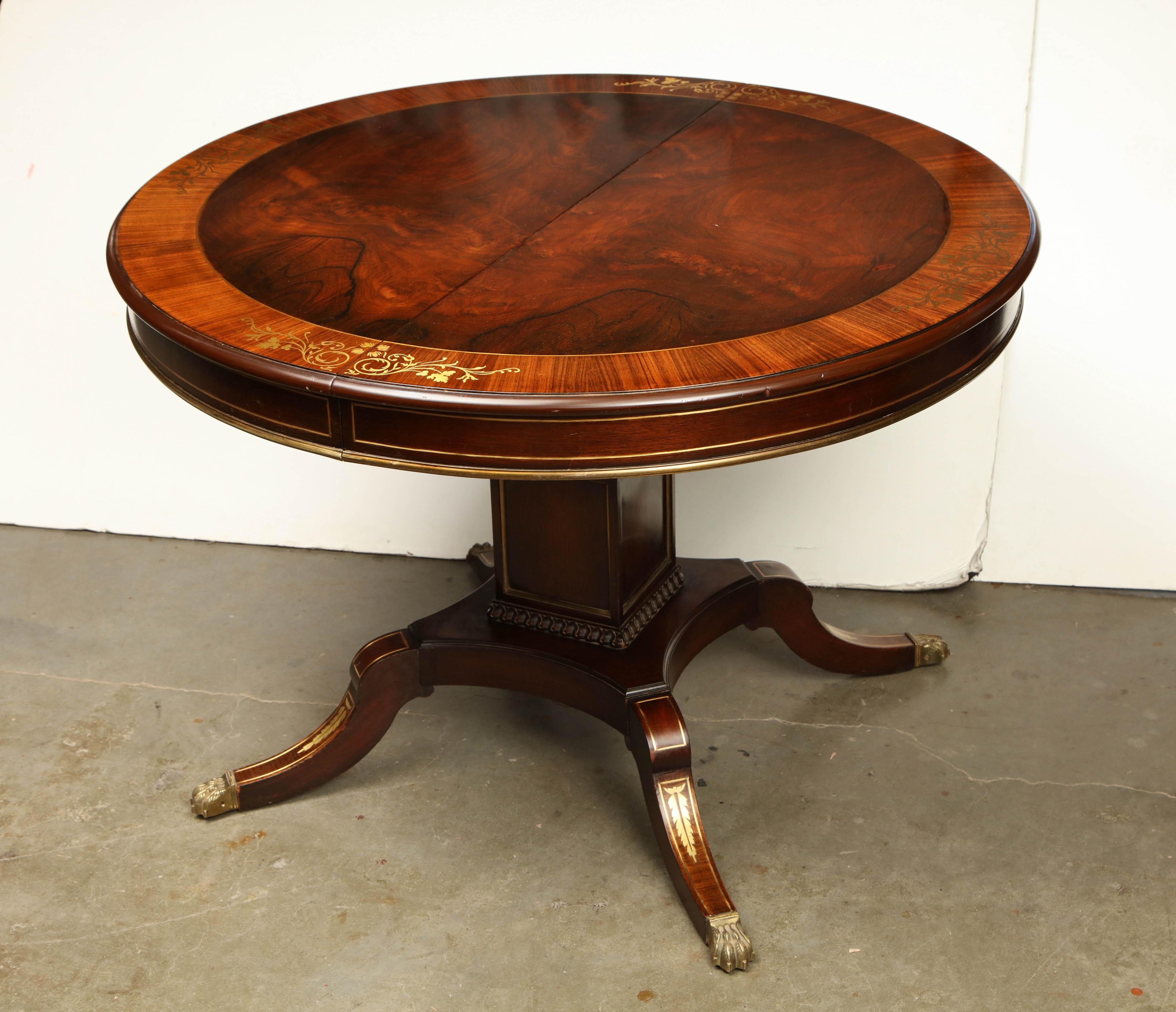 An English Regency style mahogany brass inlaid and cross banded extending dining table on a single pedestal base with four brass paw foot legs.
Measures: With one 12