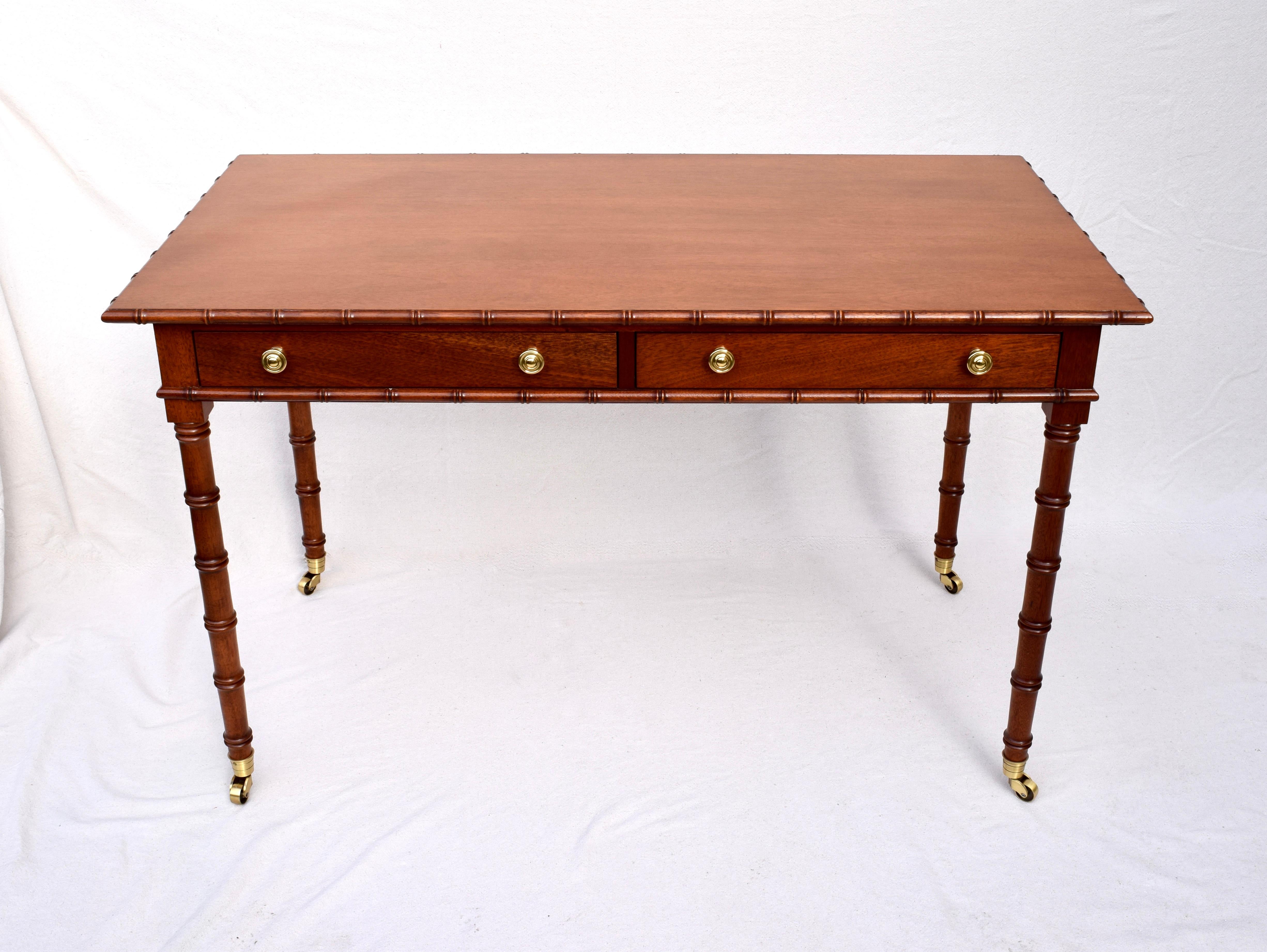 An elegant Regency style faux bamboo writing desk of solid mahogany construction on brass casters. Two generously sized drawers. Warm rubbed patina in excellent condition.