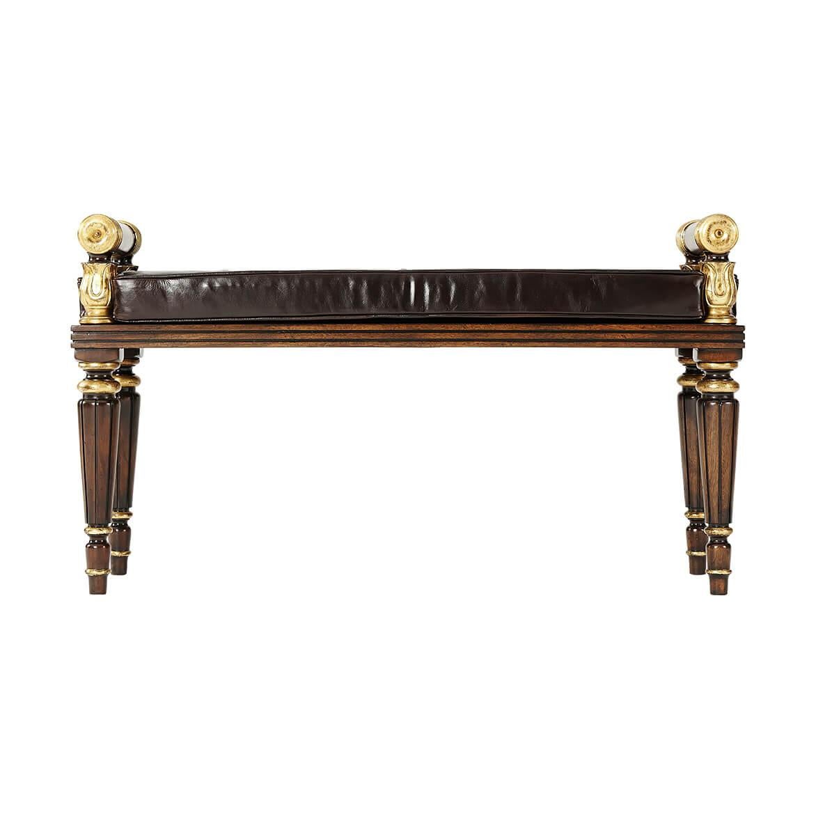 A Regency style carved mahogany and parcel-gilt hall bench, the reeded solid seat with lapette carved and scroll end supports, loose button upholstered seat cushion, on turned fluted and tapering legs. In the manner of George Bullock.