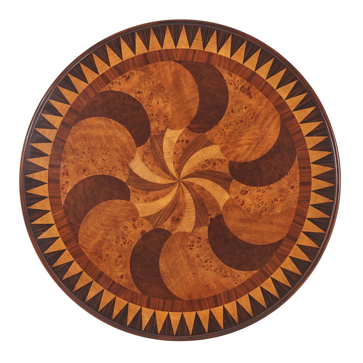 A Regency style marquetry inlaid lamp table, the circular top with swirling teardrop inlays in rosewood and burl veneers with a sunburst parquetry cross banding above a bowed frieze drawer, on inswept supports with scroll feet applied with brass