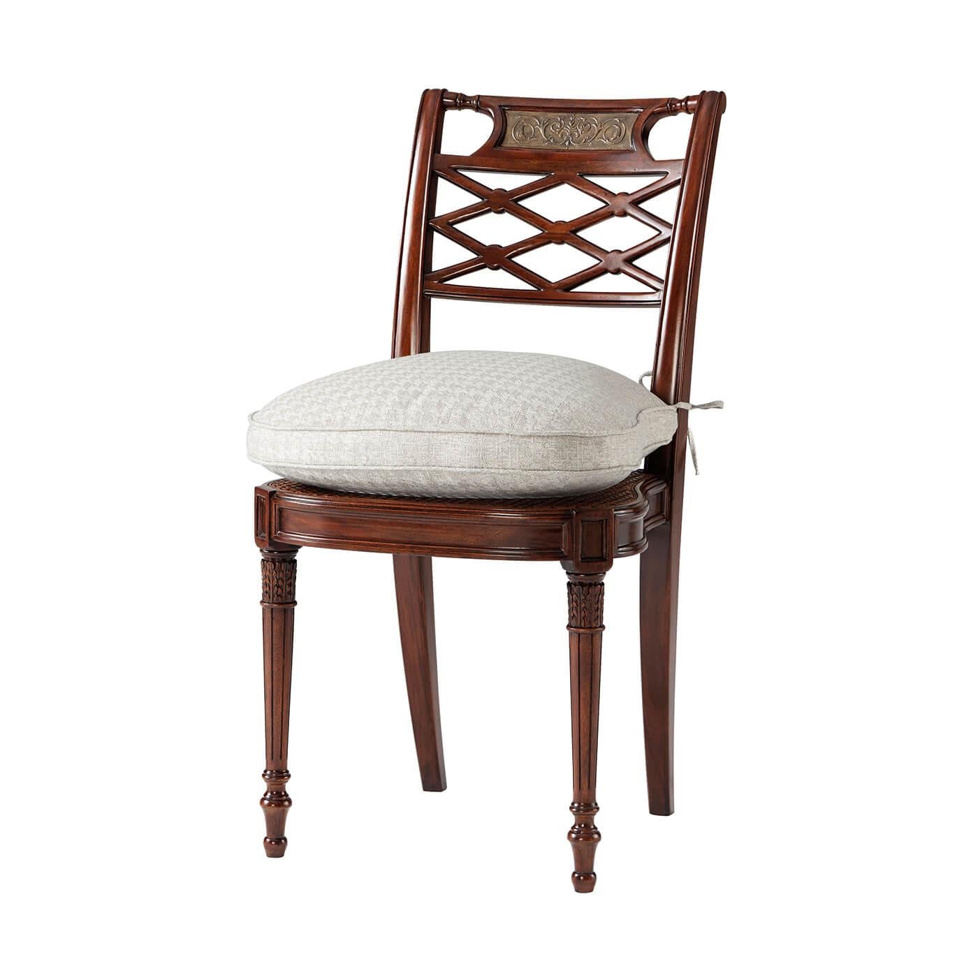 Regency style hand-carved lattice back side chair, the bar top rail inset with a 'bronzed' repoussé plaque above a lattice pierced back, on a caned seat with a tie-on cushion, on turned and fluted legs. 
Dimensions: 20
