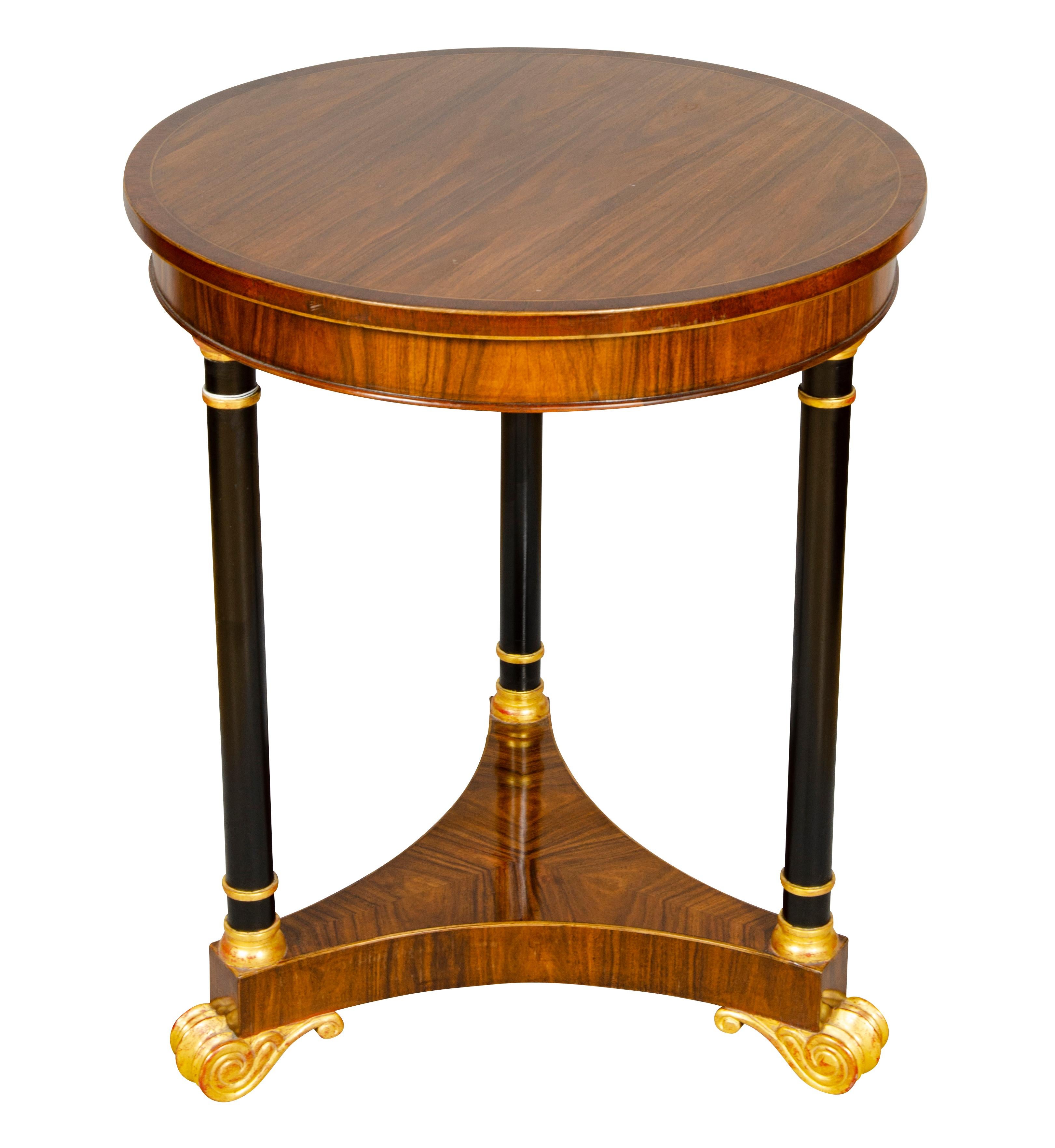 Circular banded top over a conforming frieze supported on three ebonized and gilt wood legs joined by a plinth base raised on Greek scroll feet.