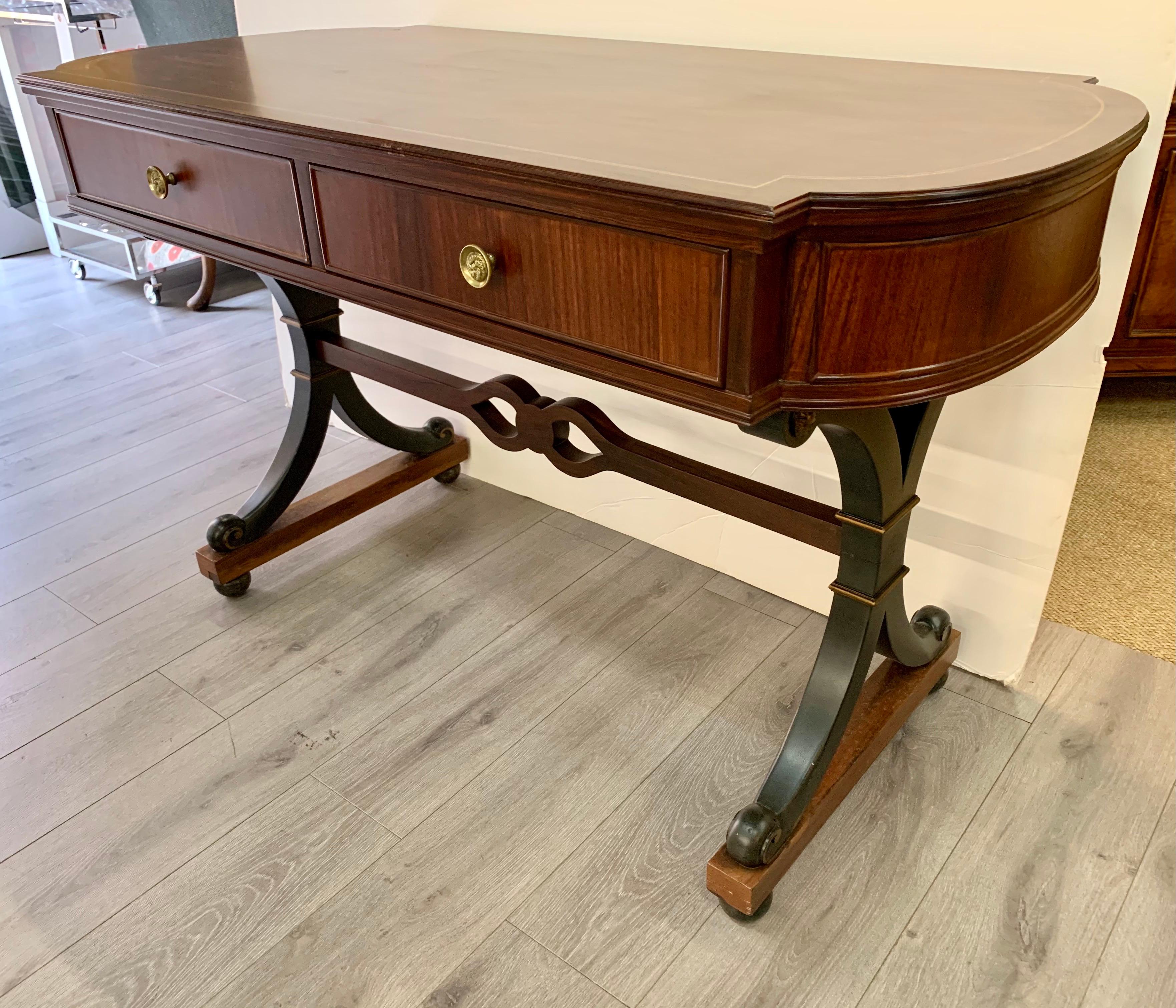 Handsome regency style mahogany desk or sofa table with line inlay on the top. It has two front drawers. Brass pulls on front and on the two faux drawers in back. It rests on black splayed legs with gold detail and carved stretcher. It is finished