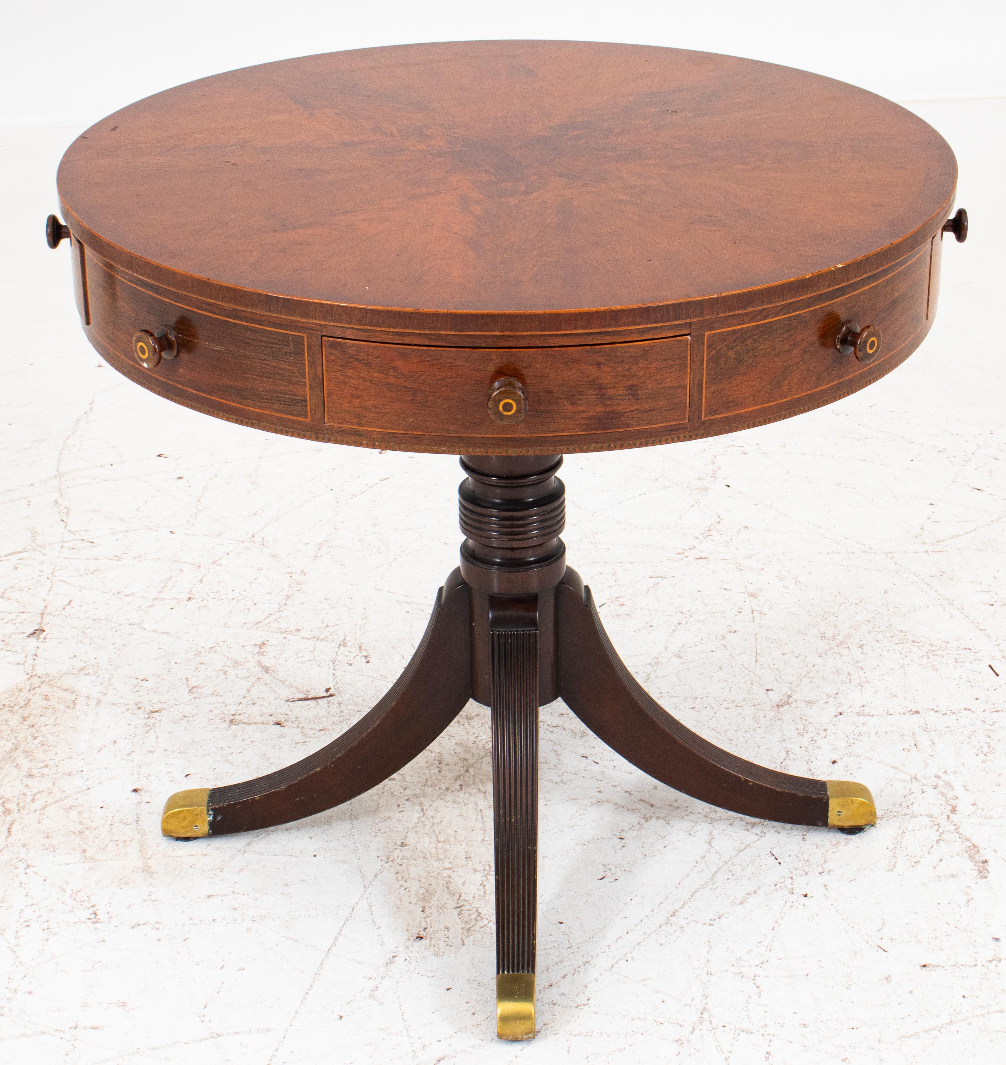 Regency style mahogany rent or drum table, circular, the apron containing four true and four false drawers, on a turned quadripedal base, reeded, and terminating in brass feet. Measures: 28.75