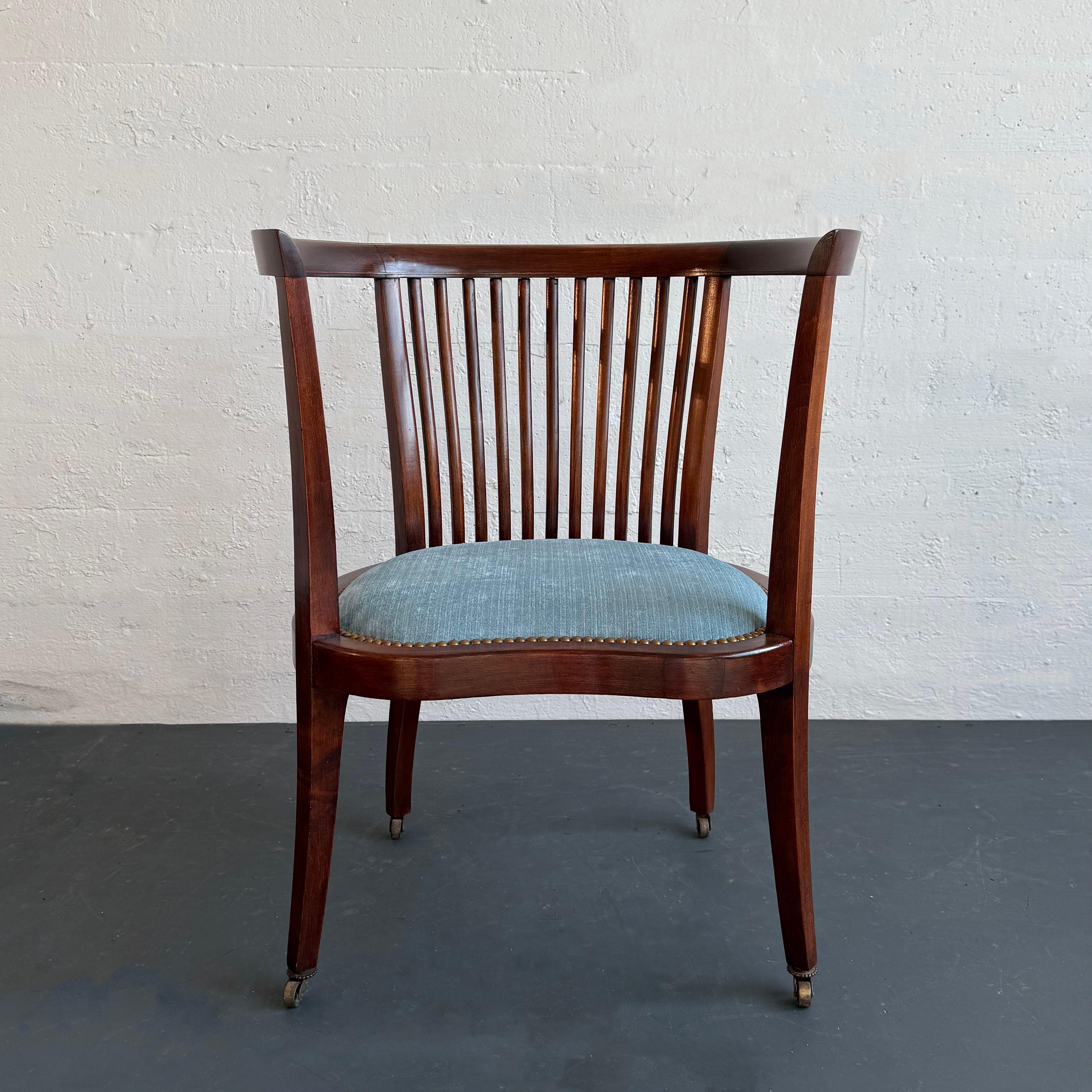 Cette chaise ancienne de style Regency, datant du début du 20e siècle, présente un cadre en acajou avec un centre en fuseau qui repose élégamment sur de minces pieds carrés effilés avec des pieds arrière balayés sur des roulettes qui roulent