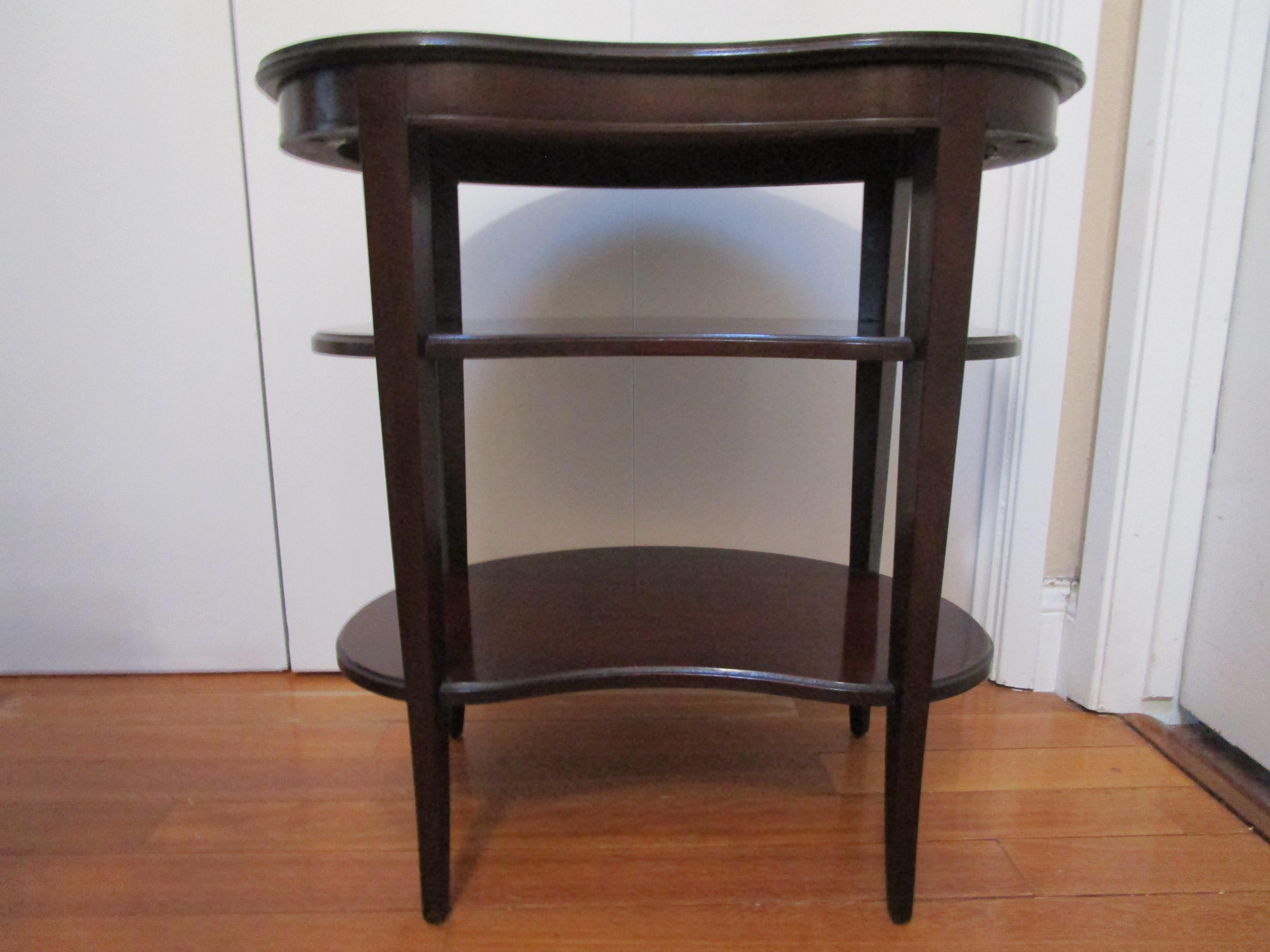 This side table is unique with its three tiers and kidney shape, echoing art deco style. This is a beautiful piece from Imperial Furniture of Grand Rapids. It is compact and functional. The Regency style mahogany kidney-form tiered side table is in