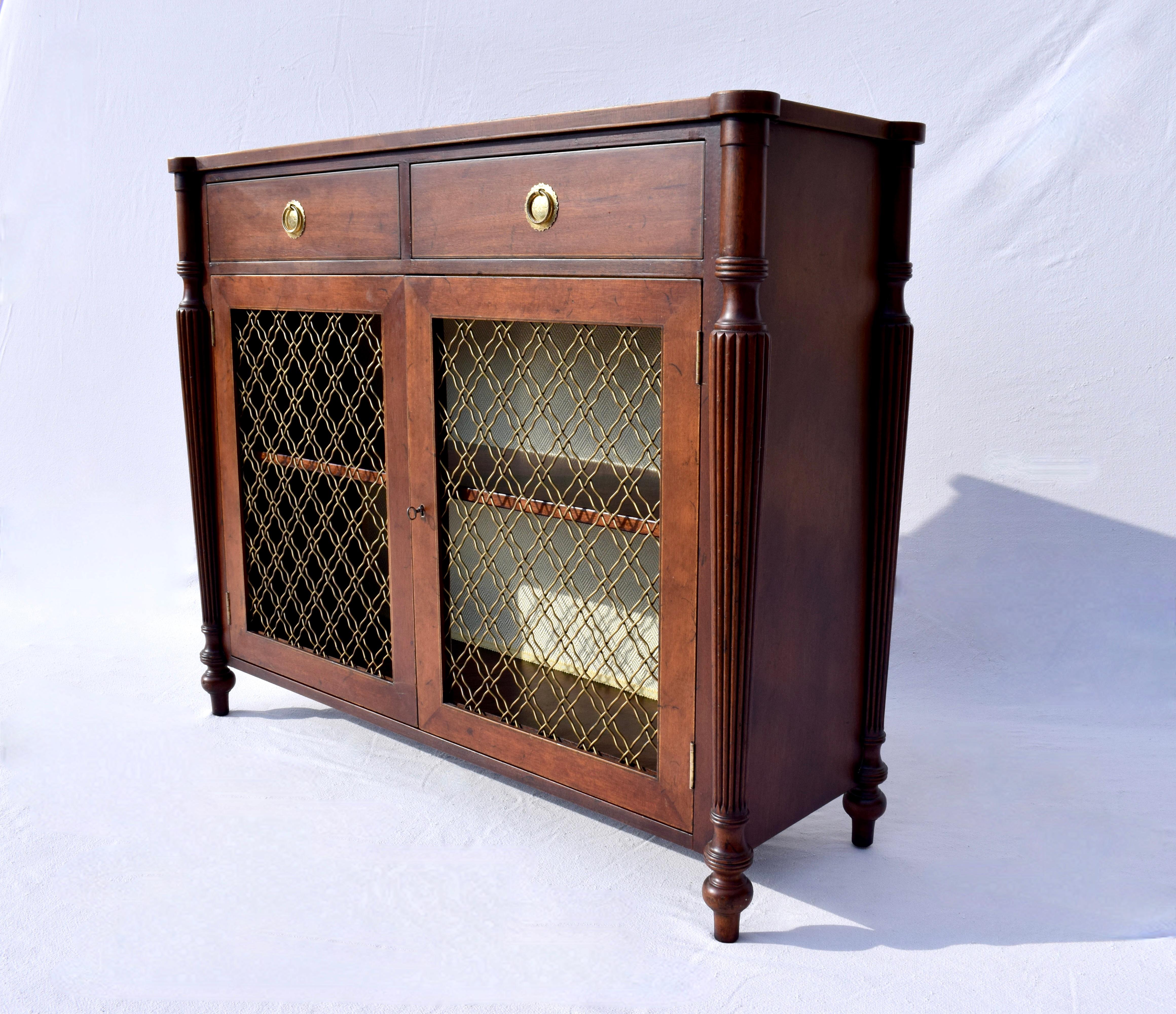 Early 20th c. Regency style Mahogany Chiffonier two drawer cabinet with pierced brass lattice front, working lock & key, tapered reed legs, single adjustable shelf and shapely turned feet. Custom textured lining to the inside back enhances the