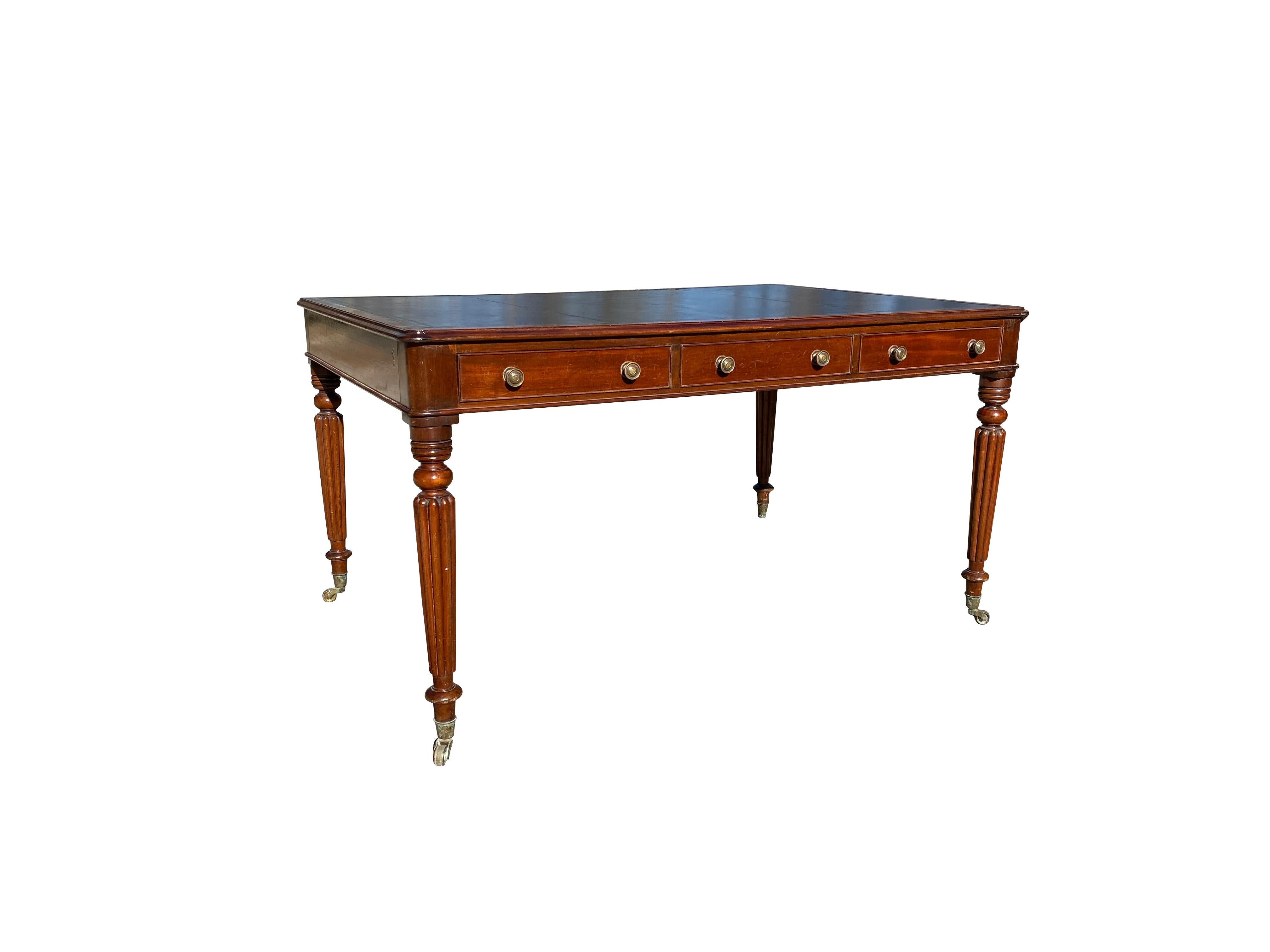 With very dark navy leather top within a banded surround over three drawers with opposing drawers on reverse, raised on circular tapered reeded legs, ending on cup casters. The leather top pictured is much lighter than it actually is.