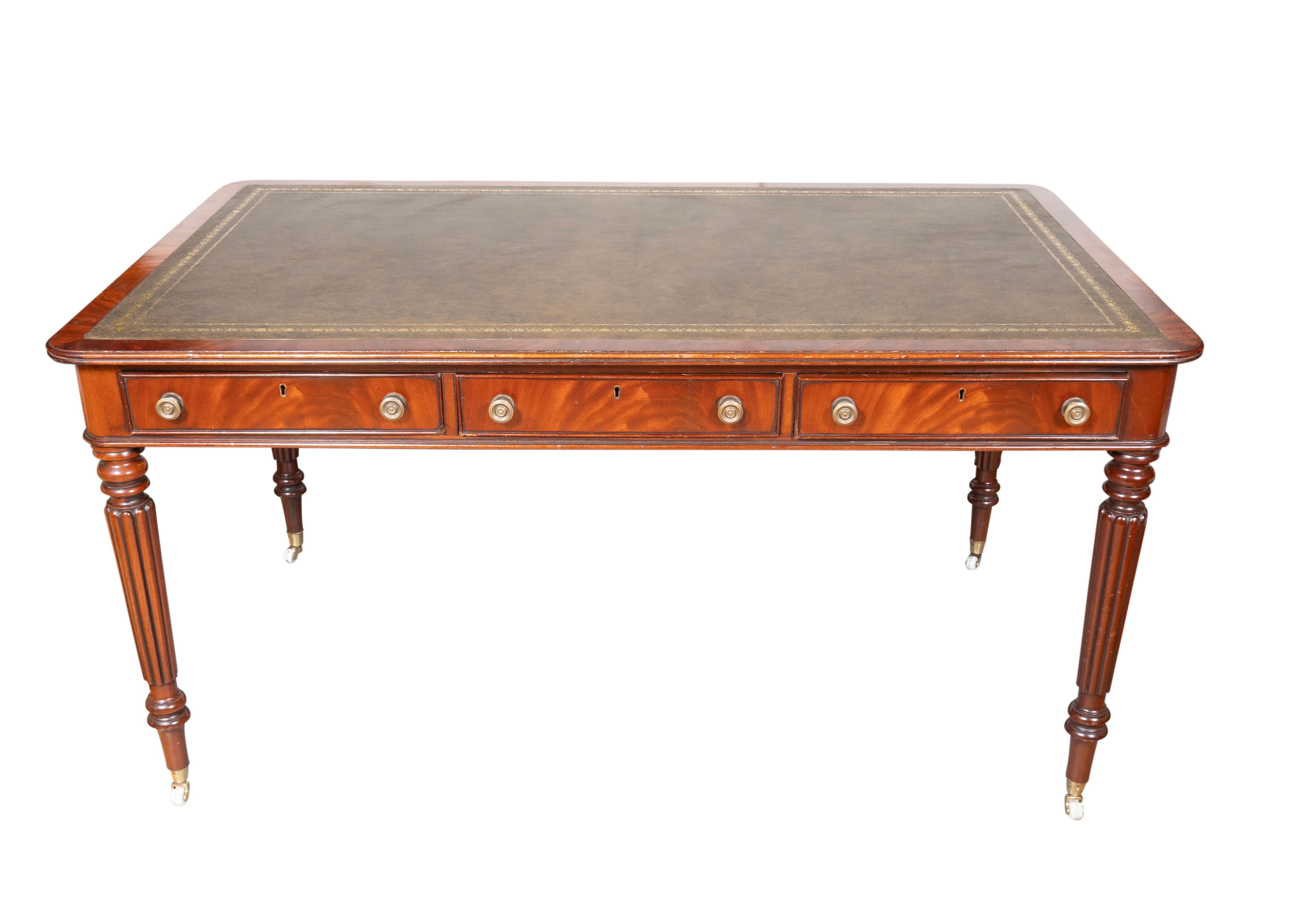 Height to underside 24.75. Rectangular top with new inset tooled olive green leather and banded edge. Three frieze drawers and three false drawers on the opposite side, with brass knobs. Circular tapered reeded legs and brass casters.