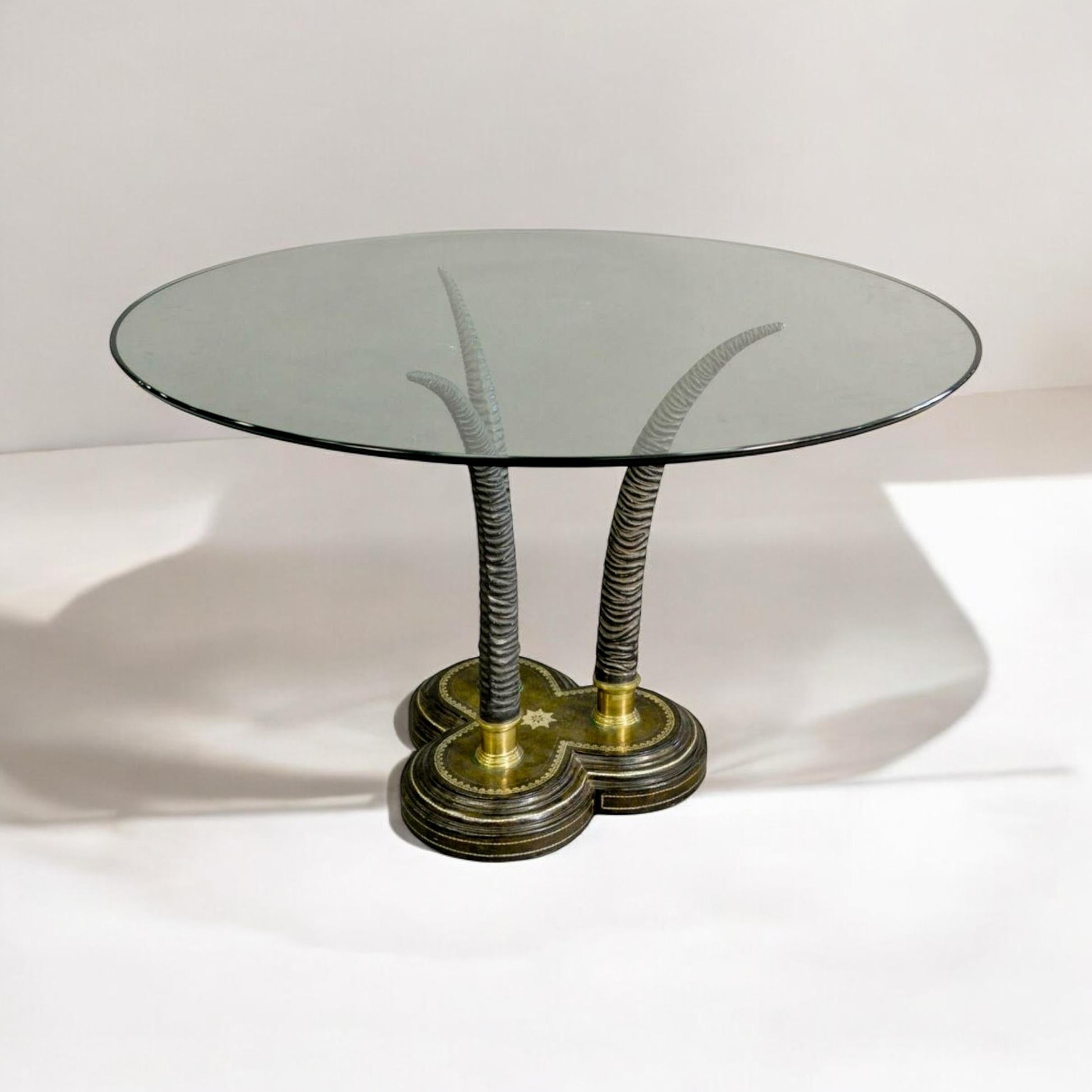 Il s'agit d'une table centrale ou d'appoint de style régence de Maitland - Smith. La base est en fonte lourde avec trois fausses cornes en métal moulé et en bronze. La base est un trèfle en cuir estampé. La base pourrait supporter un verre plus