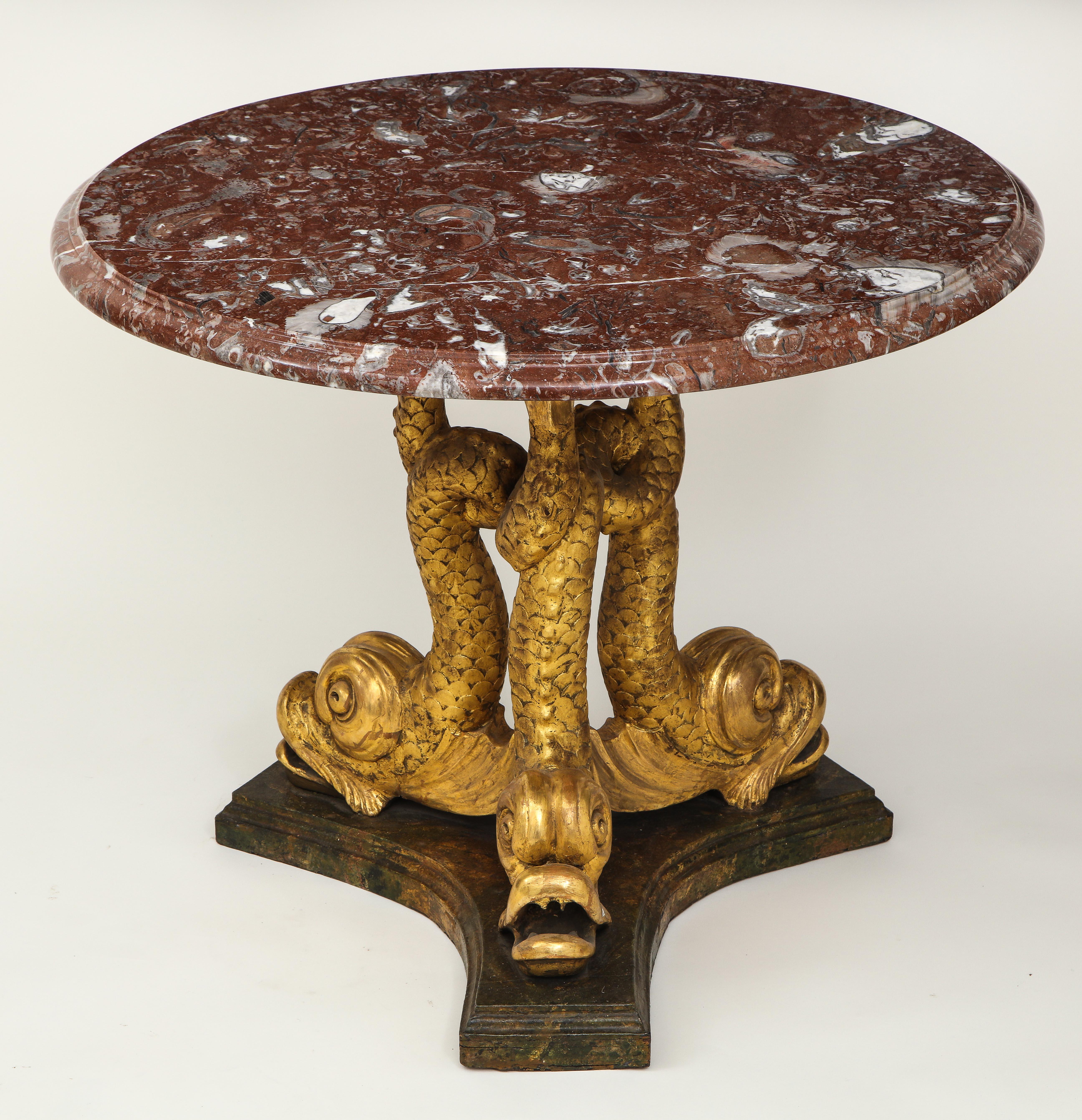 In the Brighton pavilion taste; the round rouge breccia marble top on three carved dolphin supports on a faux marble-painted tripartite base.