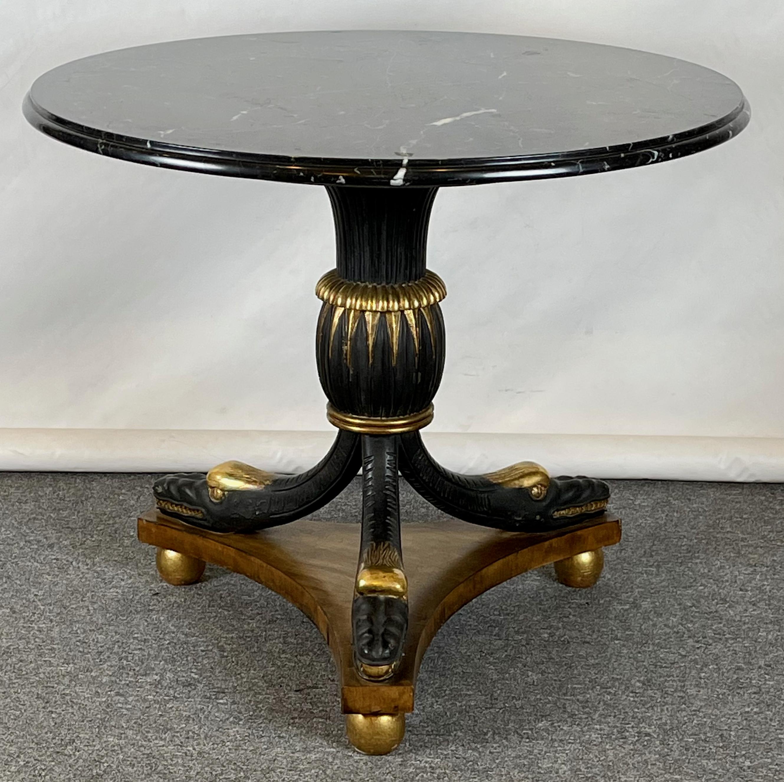 An elegant early 20th C. carved, ebonized and gilded marble top center table; the charcoal gray marble top supported by a fluted urn-shaped base resting on fancifully carved and gilded sea serpents.