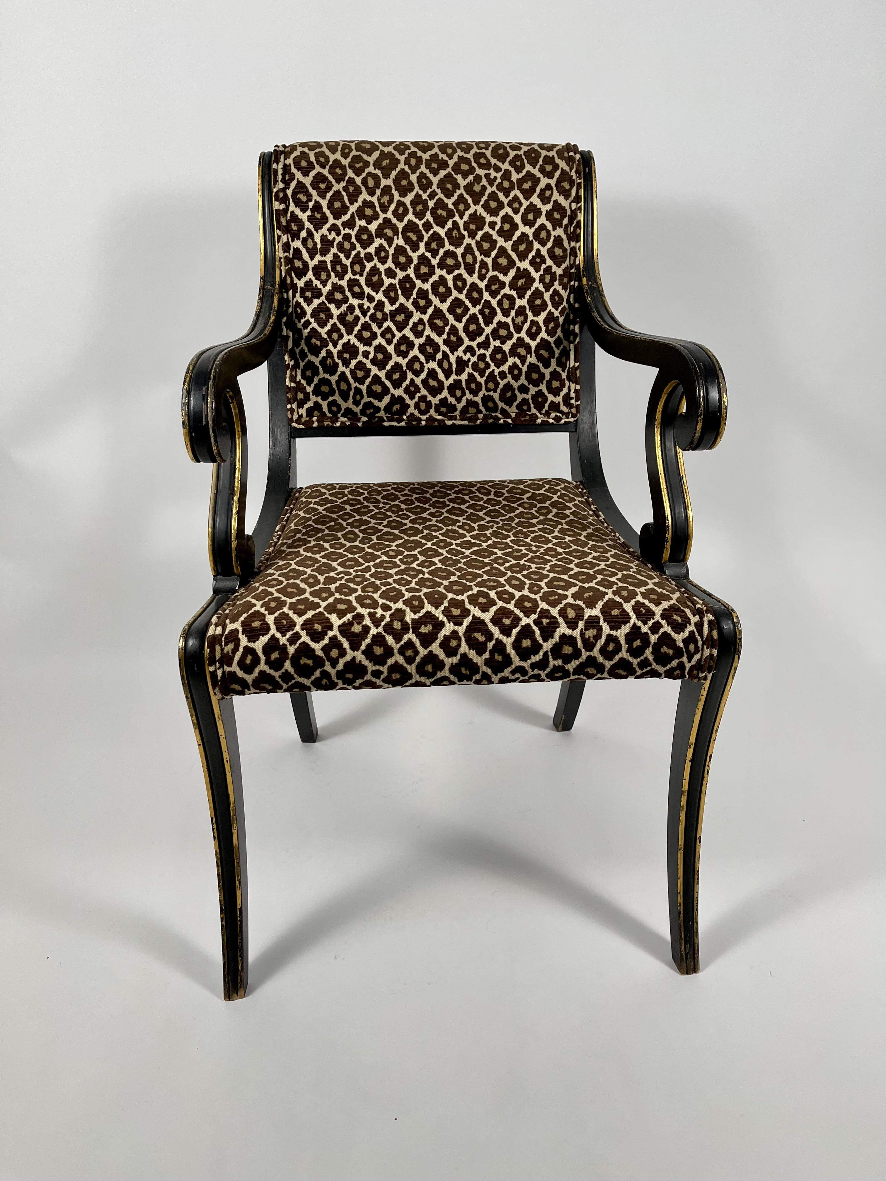 A Regency neoclassical style open arm chair, ebonized wood with parcel-gilt decoration, the upholstered back with curved crest rail and scrolled down swept arms, with upholstered seat supported by gently curving saber leg, headed with gilt brass