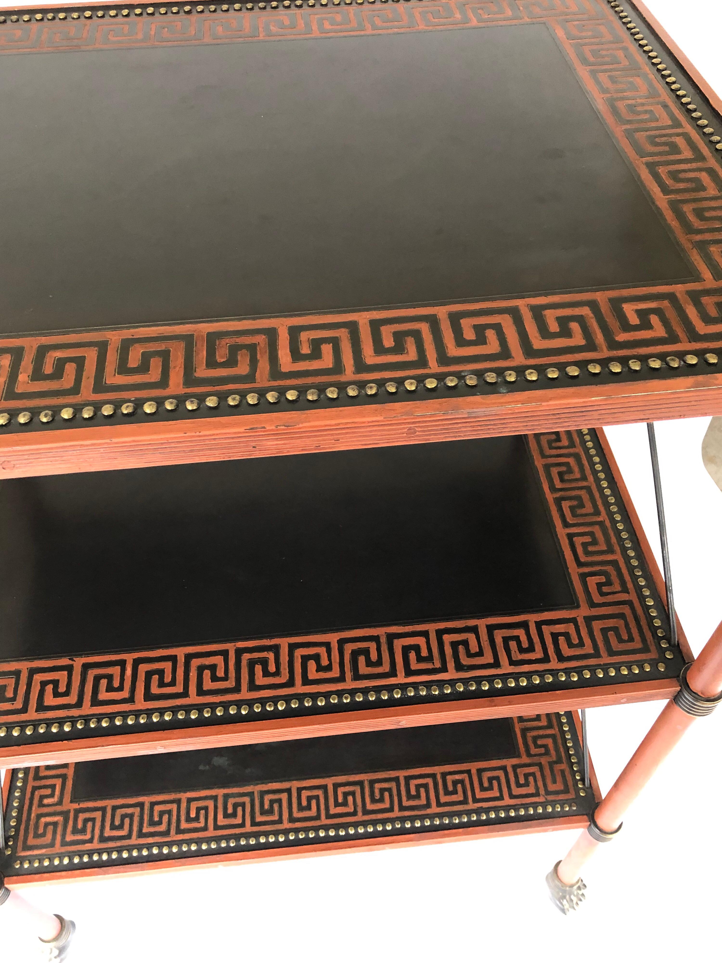 Theodore Alexander Regency style painted and lacquered 3-tier brass table. Black lacquer and decorated with siena red stringing and Greek key design, as well as nailhead decoration bordering the frame. Lion claw feet. Theodore Alexander brass label