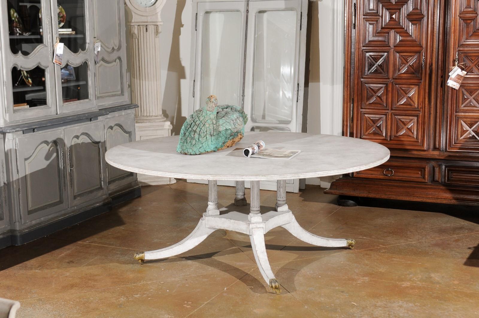 A European Regency style painted wood round top table from the 20th century, with fluted columns, brass paw feet and casters. Born in Europe, this painted table features a circular top resting on four fluted columns, raised on an in-curving low